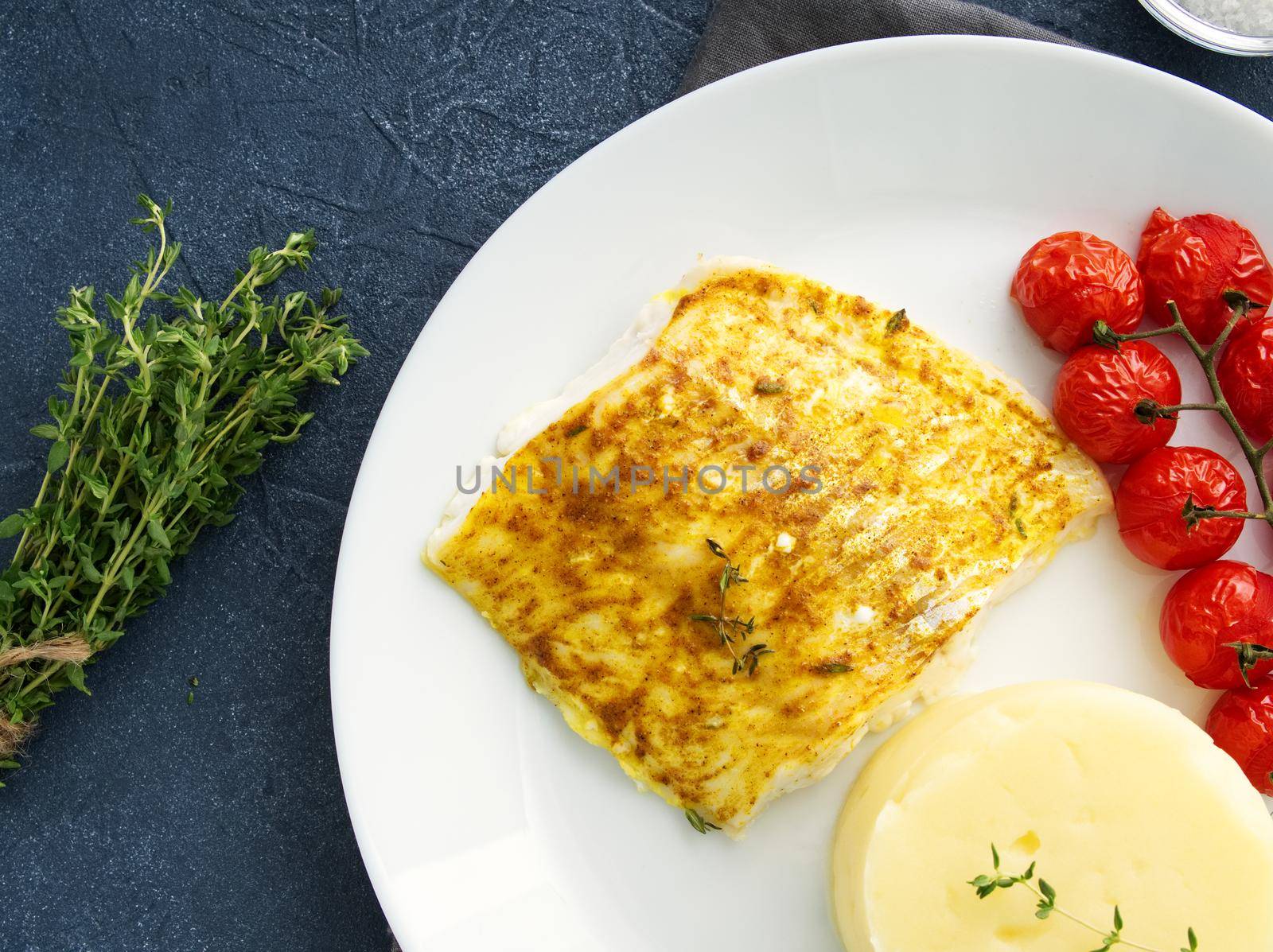 Fish cod baked in the oven with mashed potatoes, tomatoes, diet healthy food. Dark gray background, top view