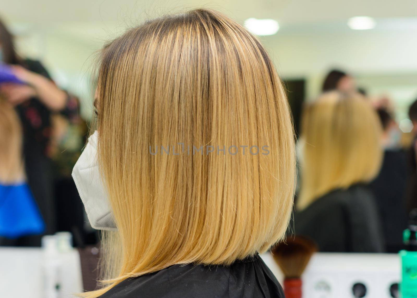 Female hairdresser holds in hand between fingers blond hair, comb and scissors close up, straightening hair tips. new