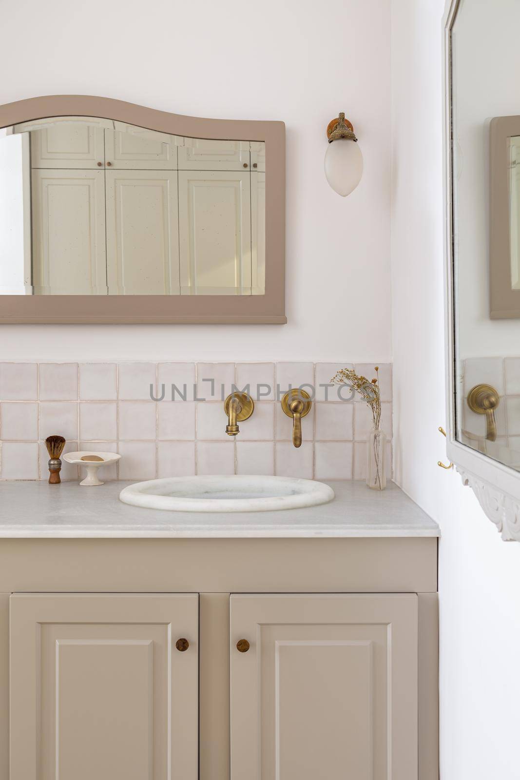 Bathroom decorated in beige color with sinks, golden faucets and vintage mirror. Interior of restroom in retro or classic style