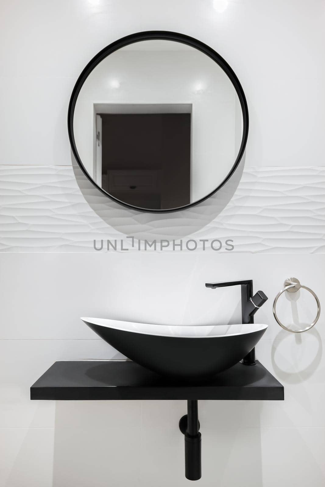White tiled bathroom with black faucet and basin and round mirror. Modern and minimalist style. by apavlin