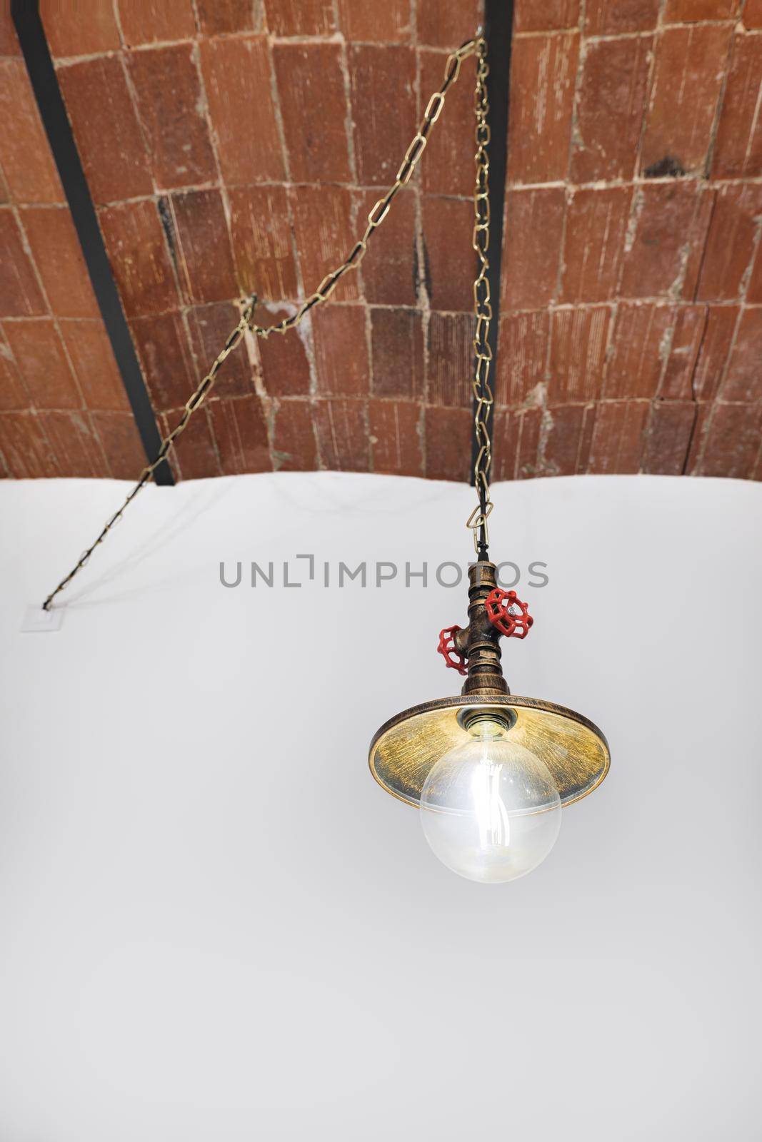 Vintage lamp of plumbing style hanging on chain on background of white wall with brick ceilings