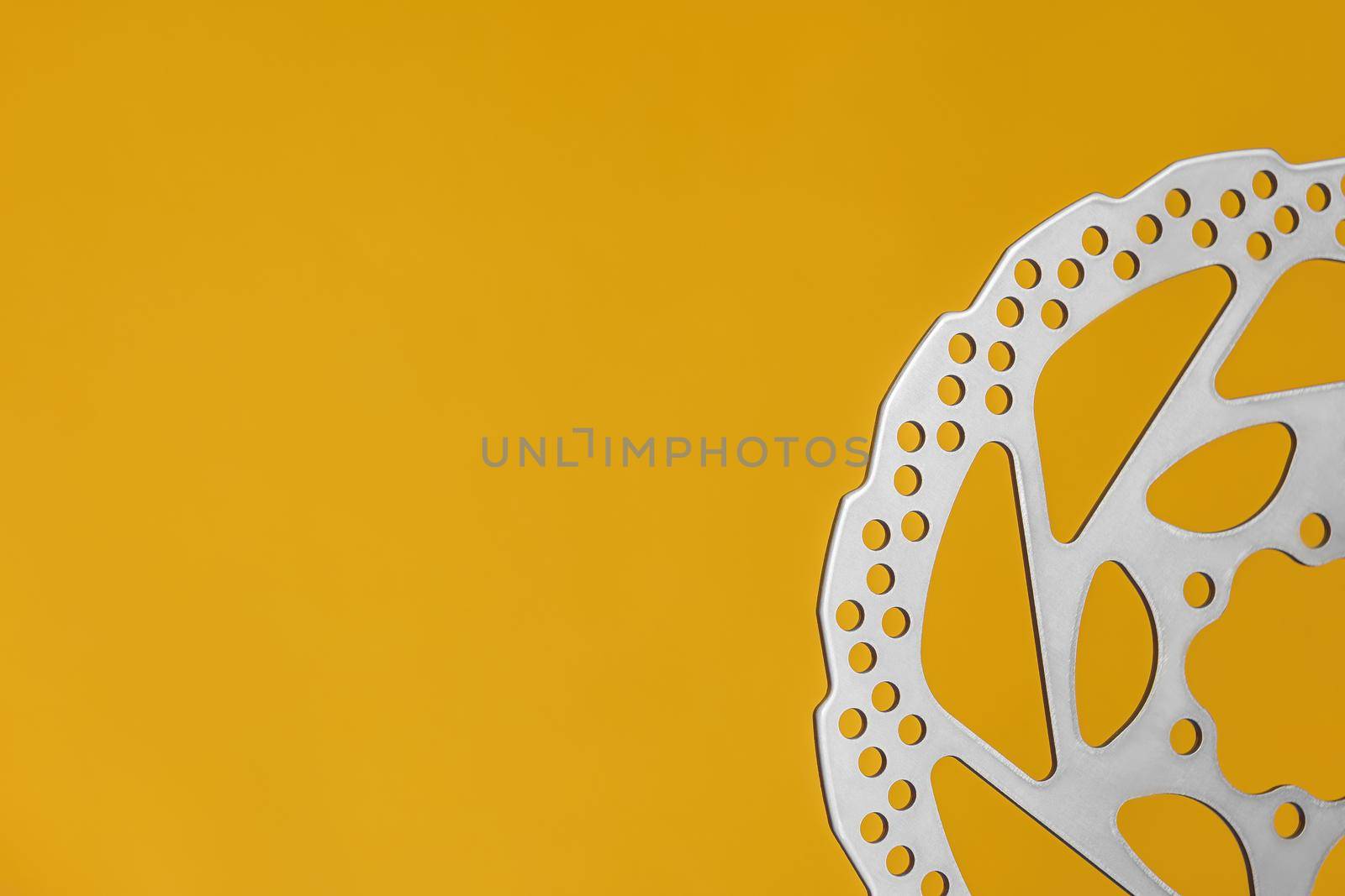 Half of new brake disc for bicycle hydraulic brakes with yellow background and copy space.