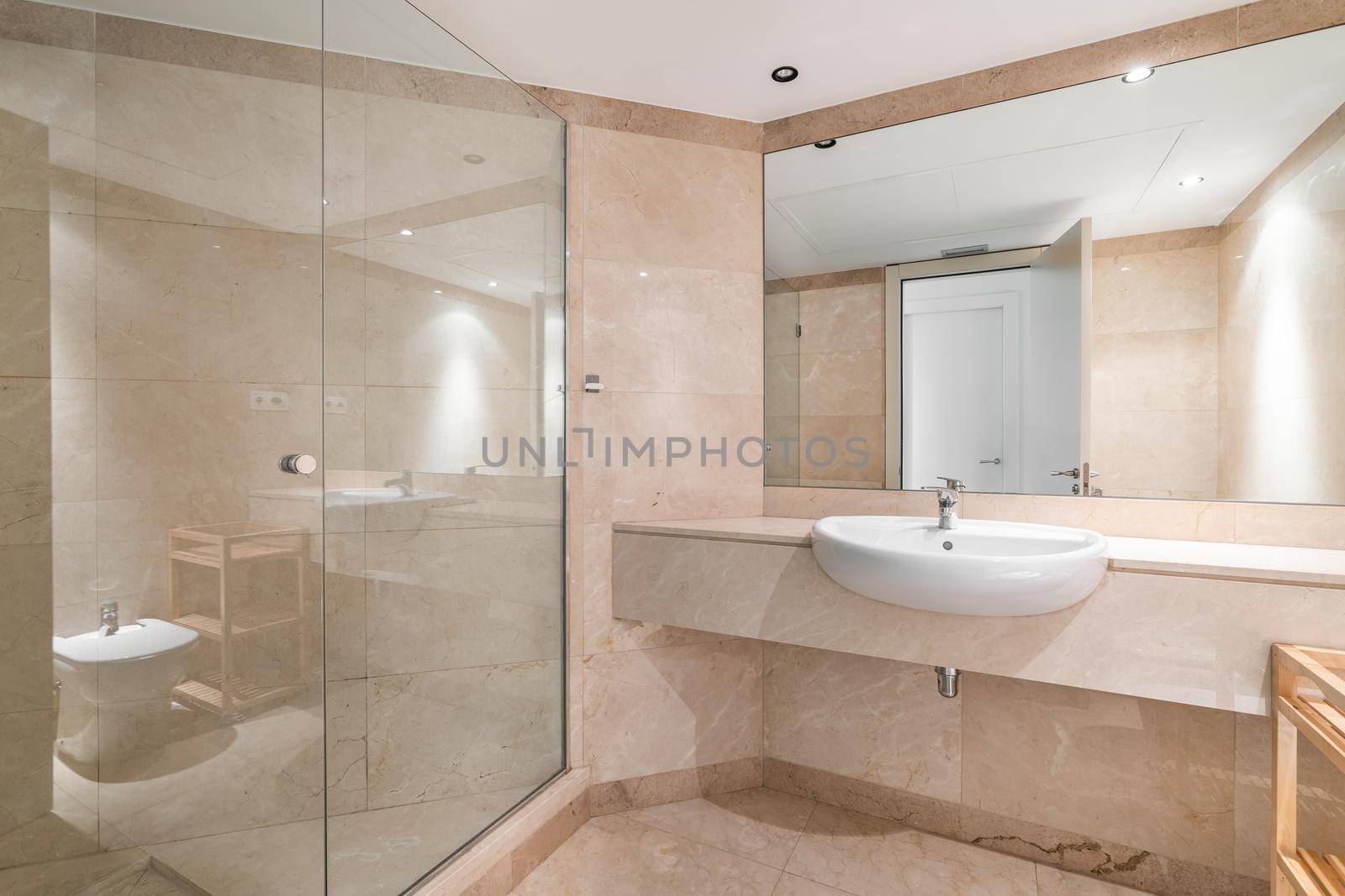 Interior of a peach bathroom in classic design, with shower zone, marble finishing and large mirror.