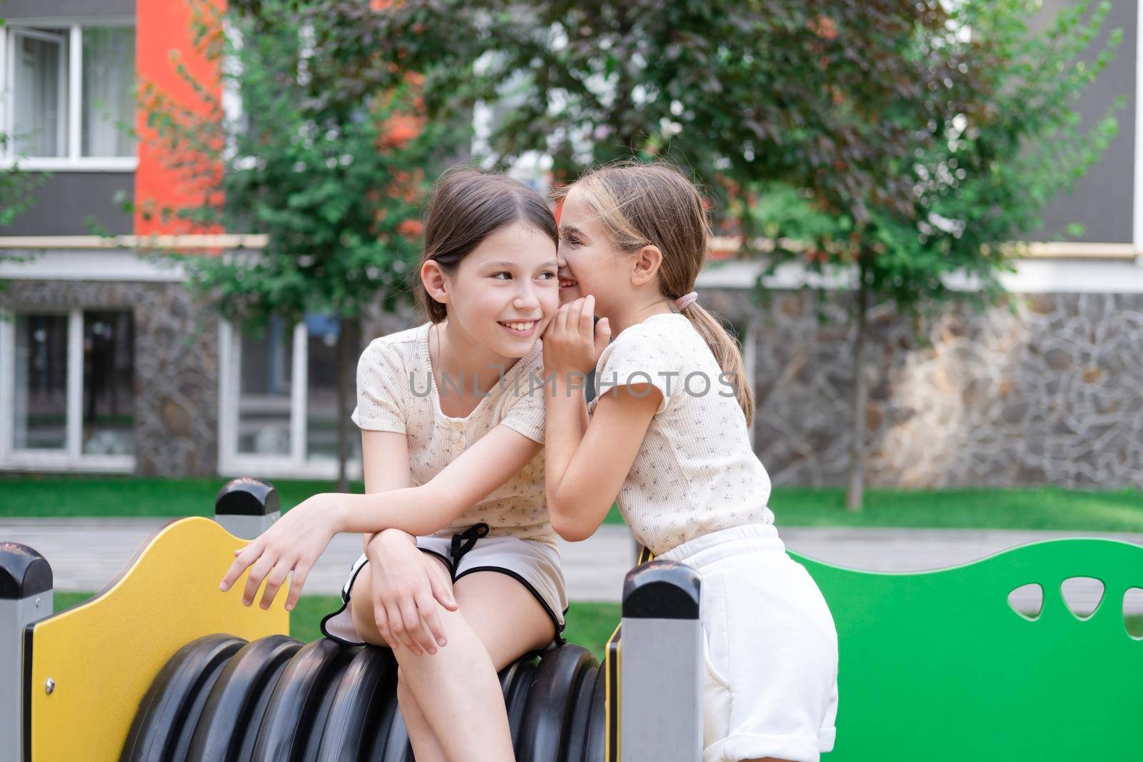 kids outdoors having fun on modern playground with new colorful equipment. sisterhood, friendship. two charming girls playing outdoors. sister, bffs, friends.