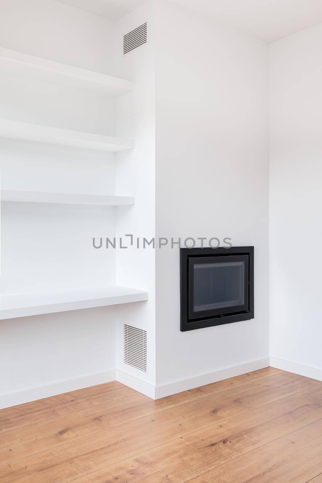 Part of white living room in a newly renovated apartment with a fireplace, shelves and vents.