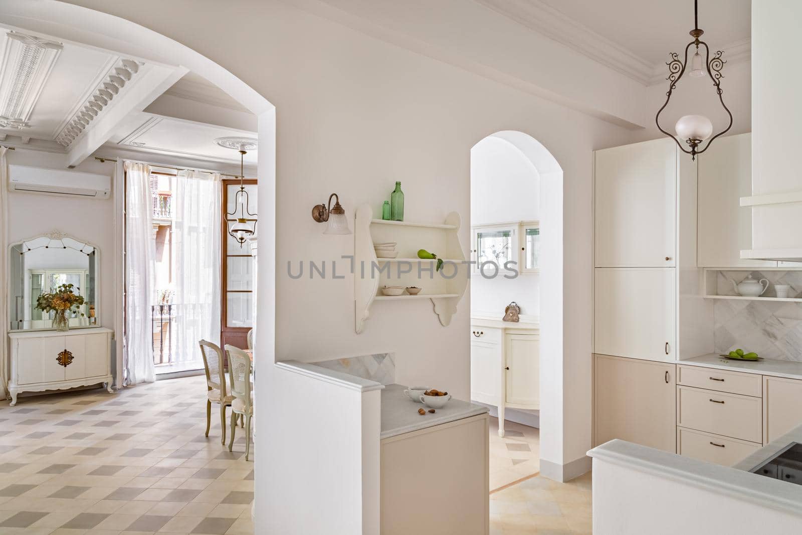 Classic style apartment with view to kitchen and living room with tile floor, light furniture and vintage chandelier.