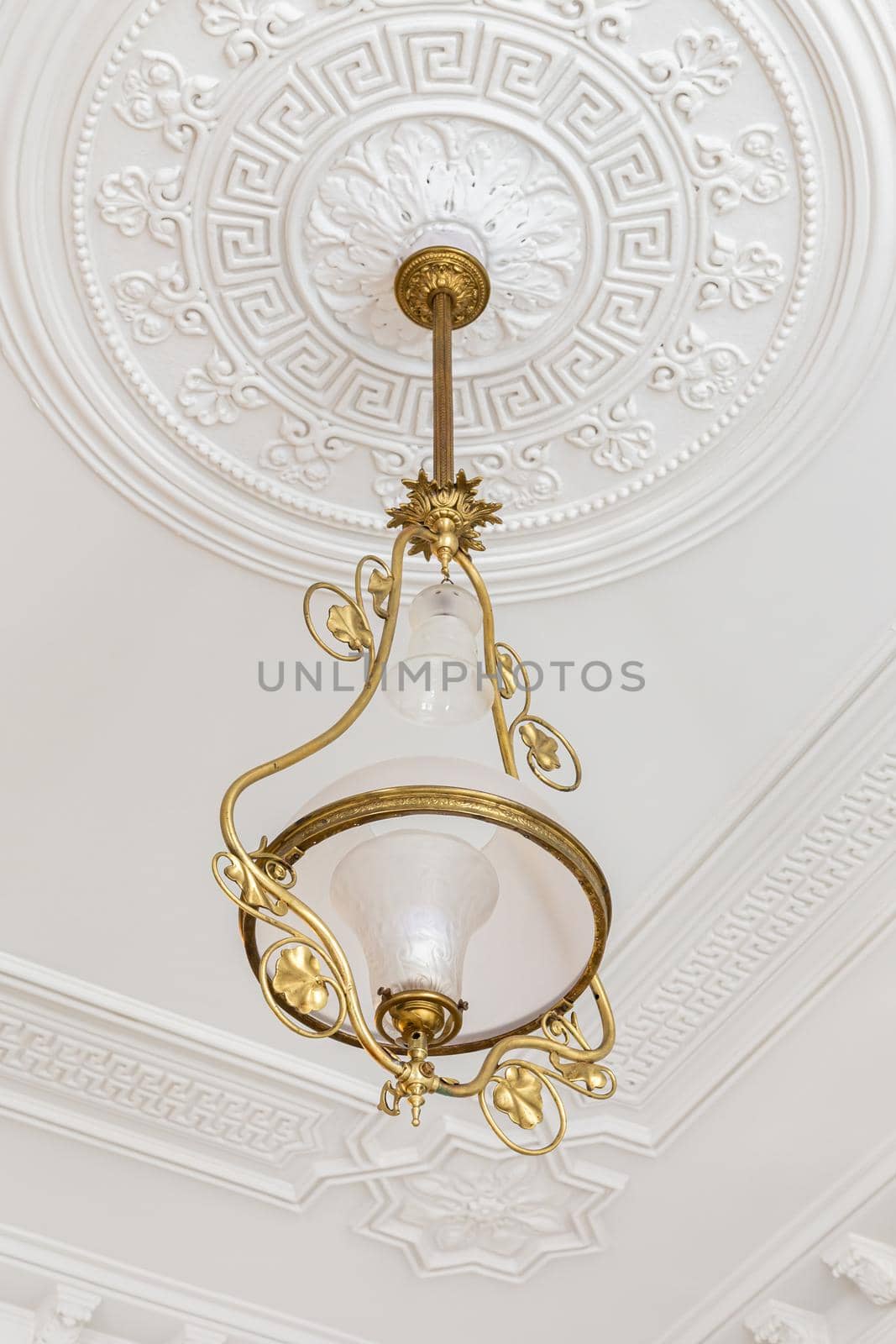 Vintage chandelier in the interior of white room with stucco molding on the ceiling.