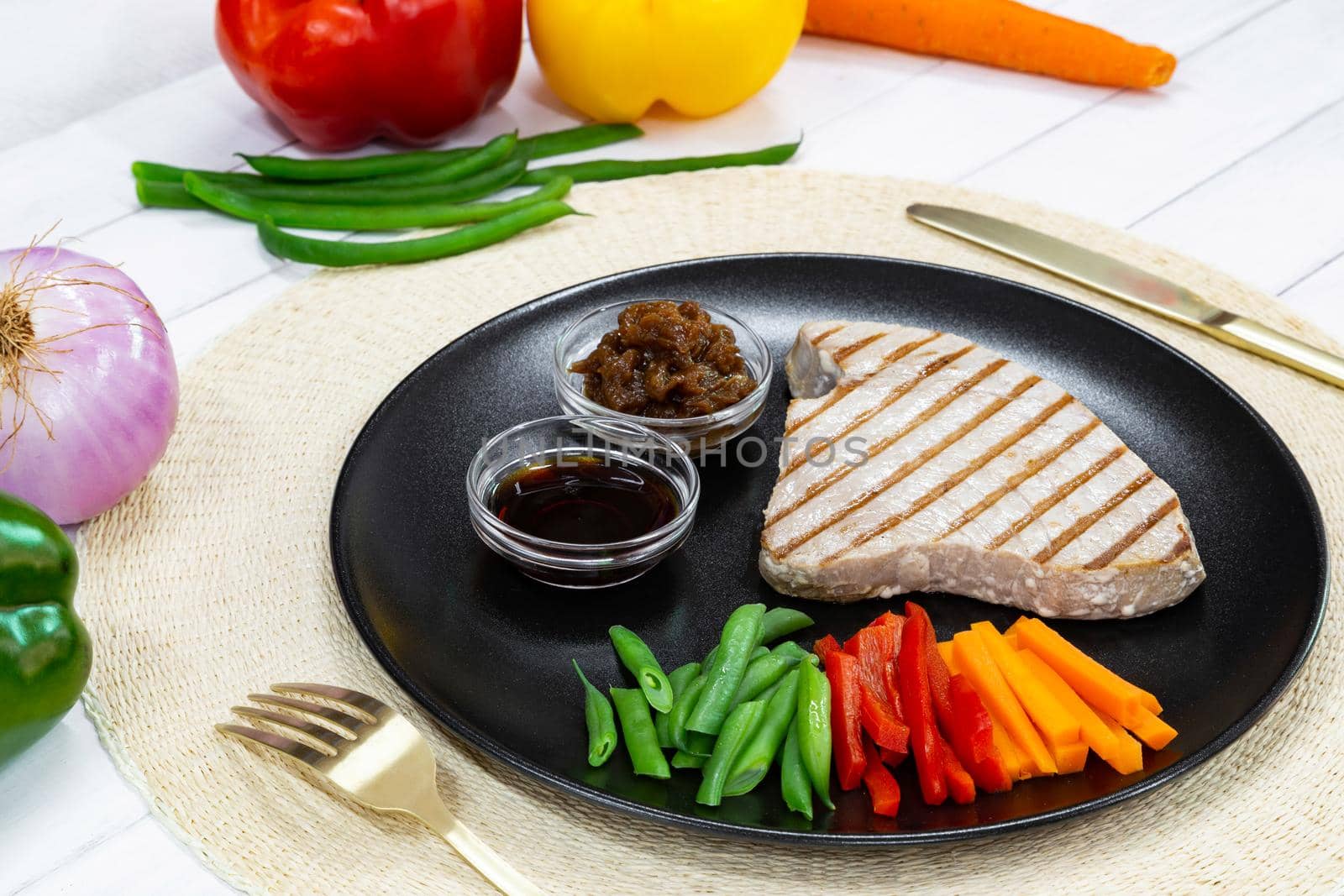 Grilled tuna steak on black plate with sauce, caramelized onion and fresh vegetables by apavlin