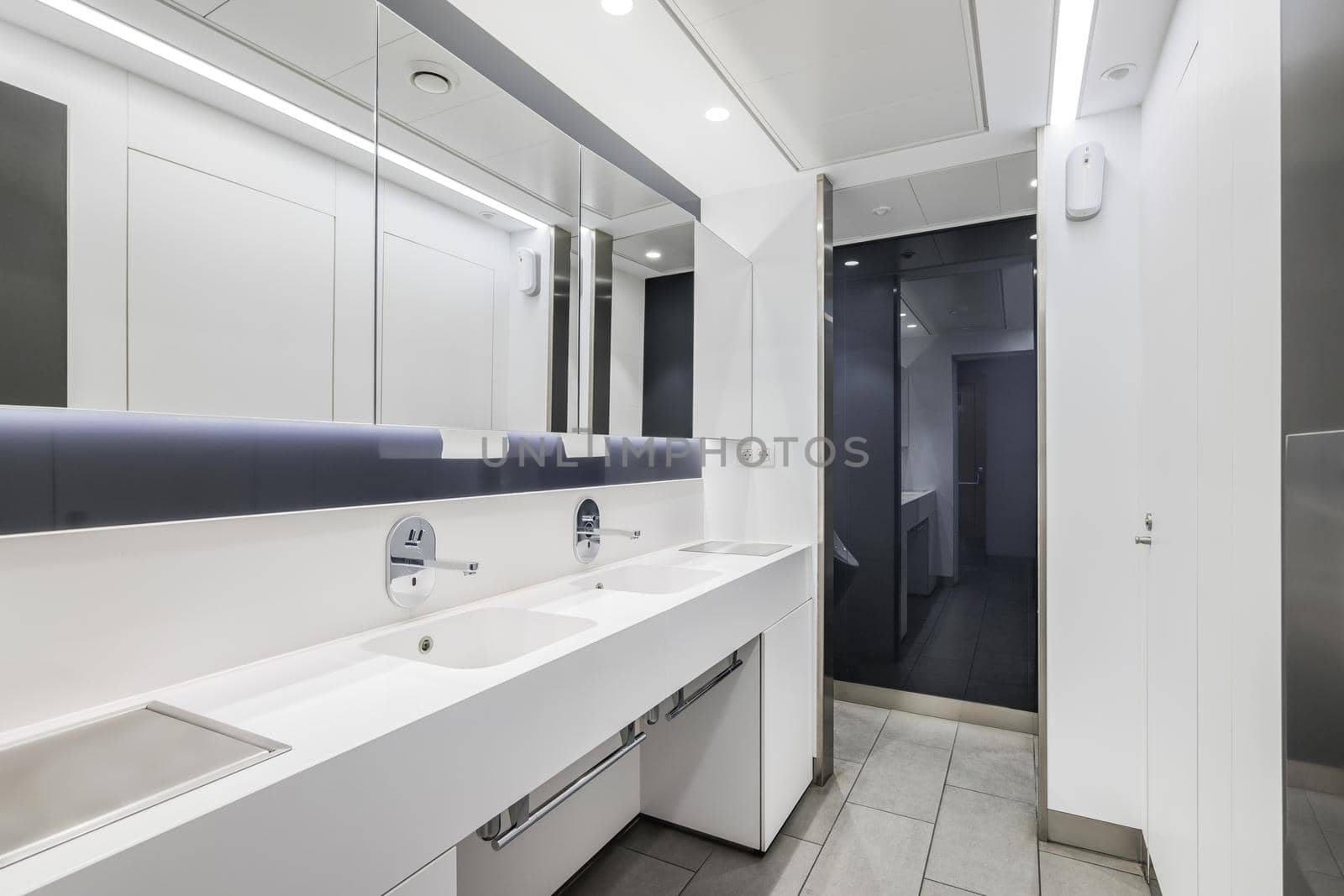 Public or office interior of male restroom with sinks and big mirror. Modern design bathroom in white color