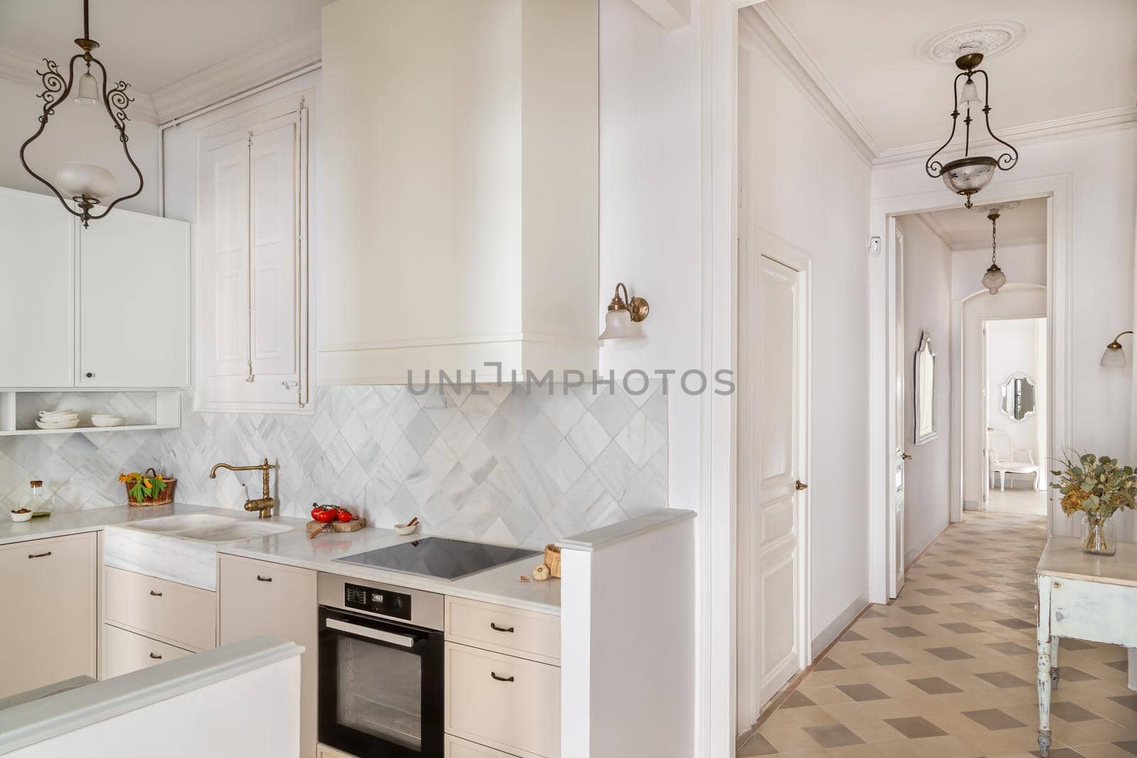 Hallway and kitchen with white furniture and tiles in bright cottage. Interior decorated in retro style with vintage chandeliers