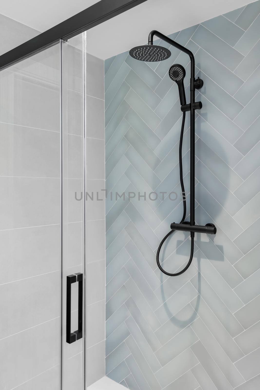 Modern shower zone with rain head, hand held shower and glass door. Light blue and white tiles in the bathroom.