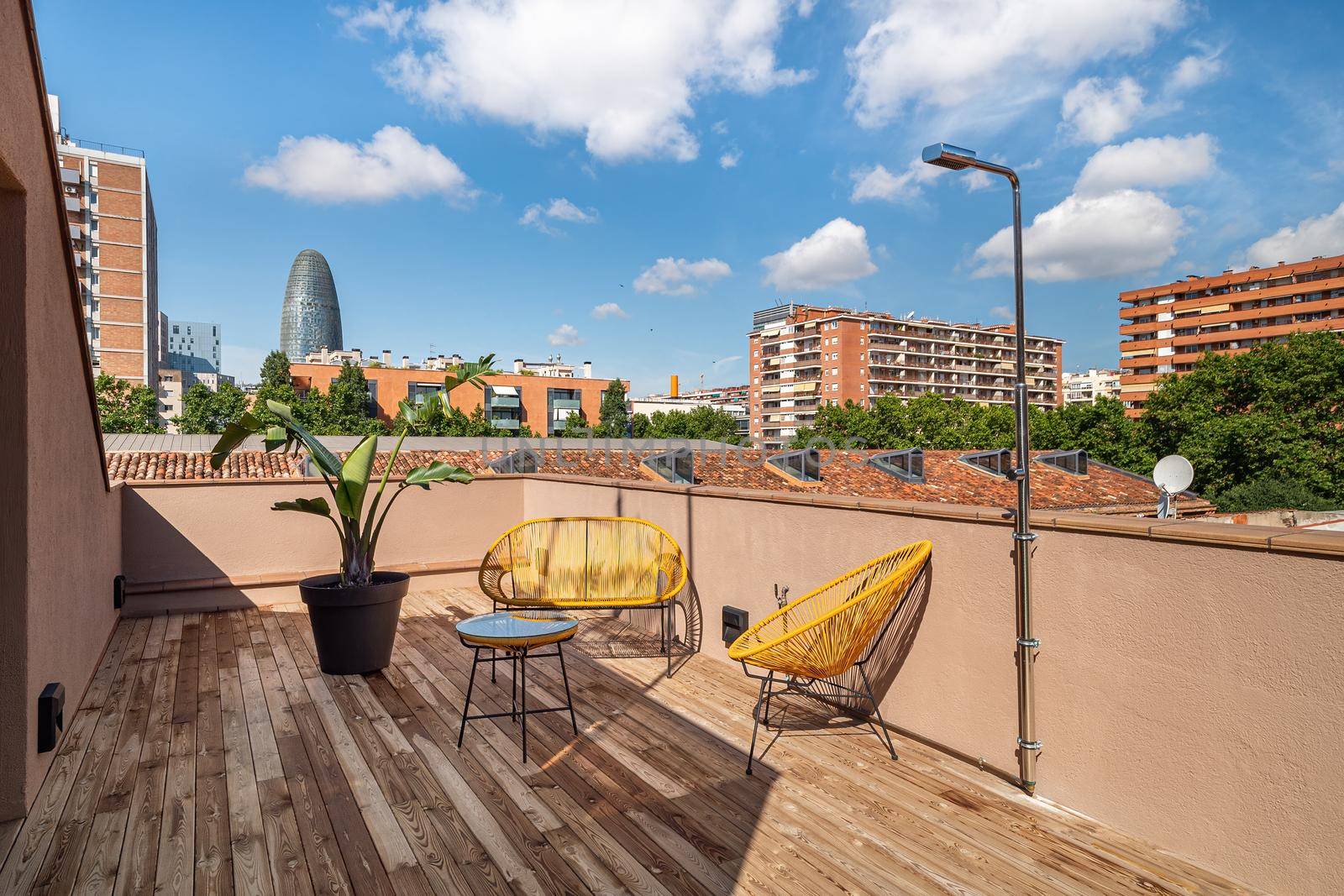 Bright terrace with yellow exterior chairs, wooden floor, shower and amazing view of area of Poblenou, old industrial district converted into new modern neighbourhood in Barcelona, Spain by apavlin