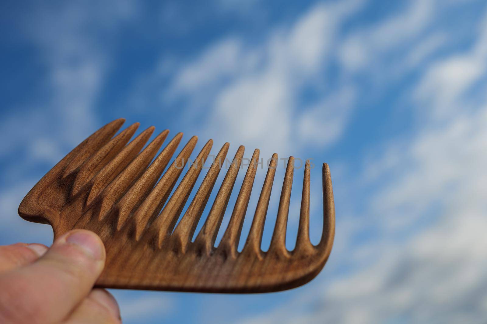 Handmade wooden comb for scalp massage and hair combing at blue sky background. Hair care concept. by apavlin