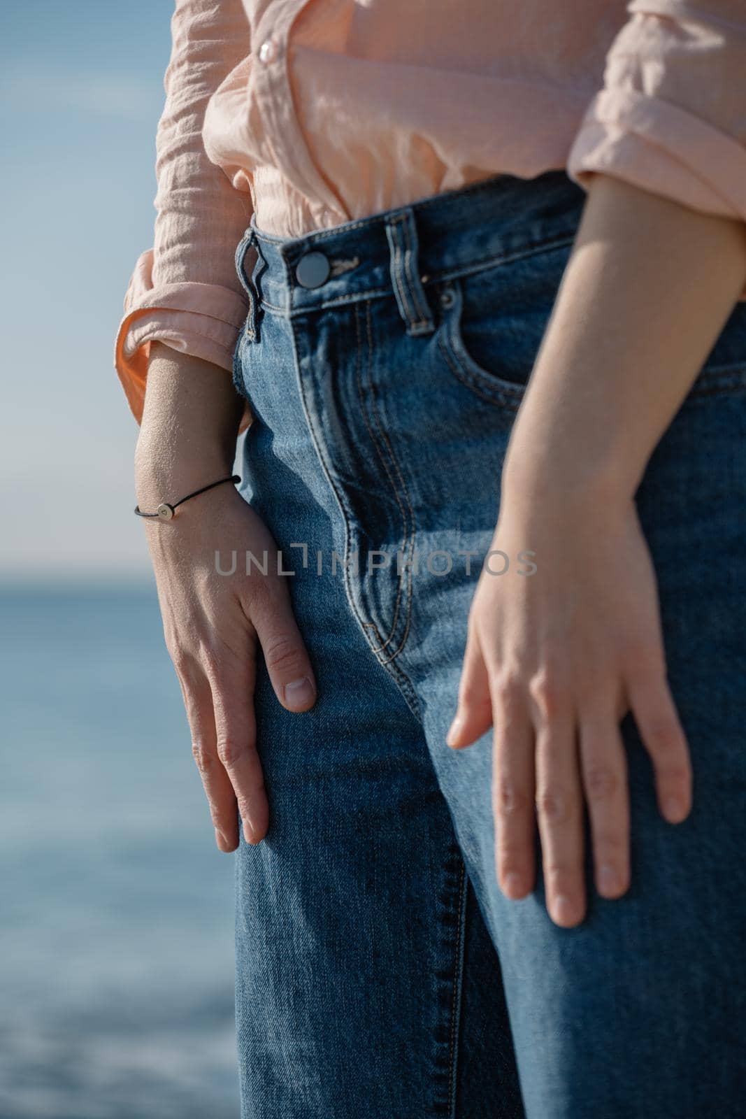 Woman standing at the sea background, holding her hands on jeans. Relaxing and calm concept