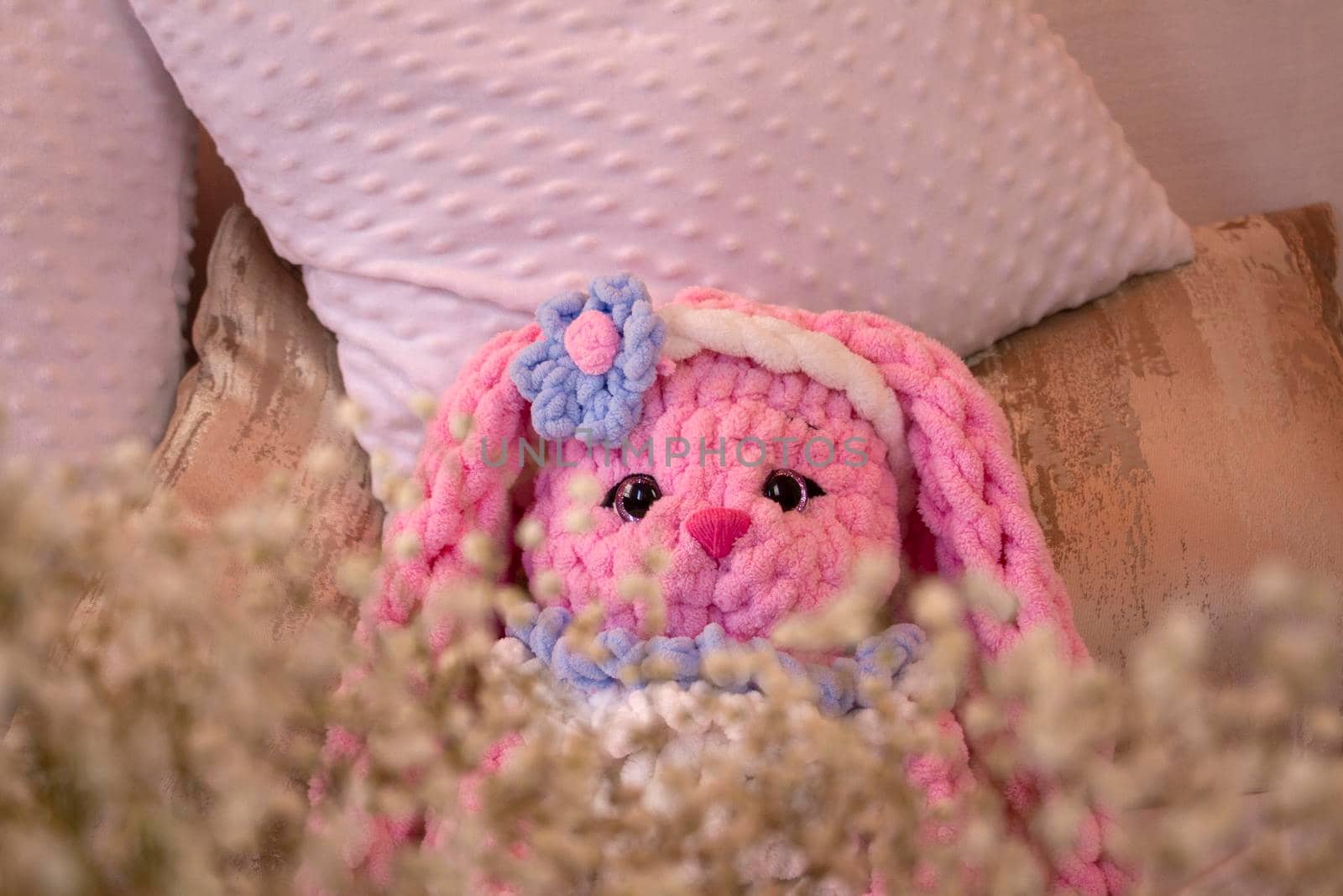 pink rabbit knitted toy sits on the sofa. Animal crochet. Amigurumi. Place for text by Hitachin