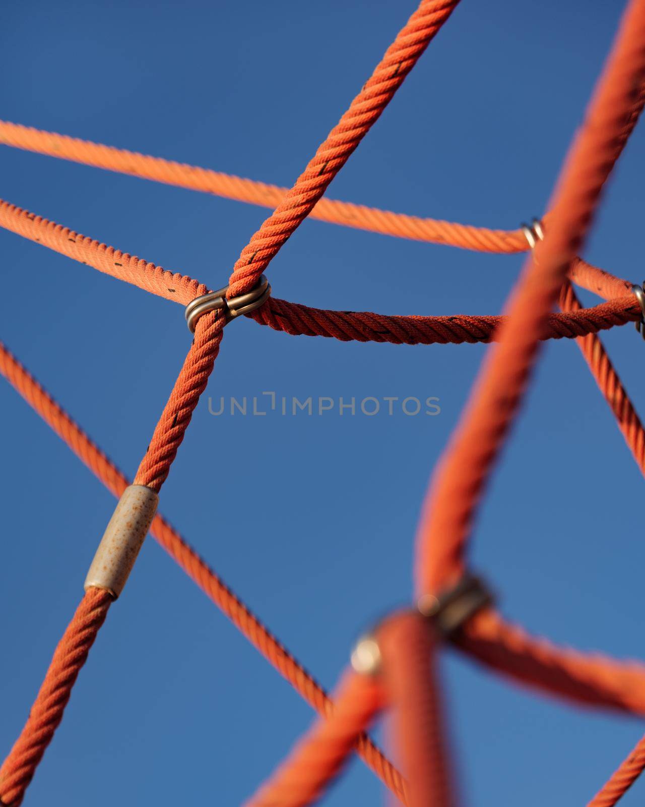 Abstract detail picture of climbing frame with red ropes and blue sky in playground. by apavlin