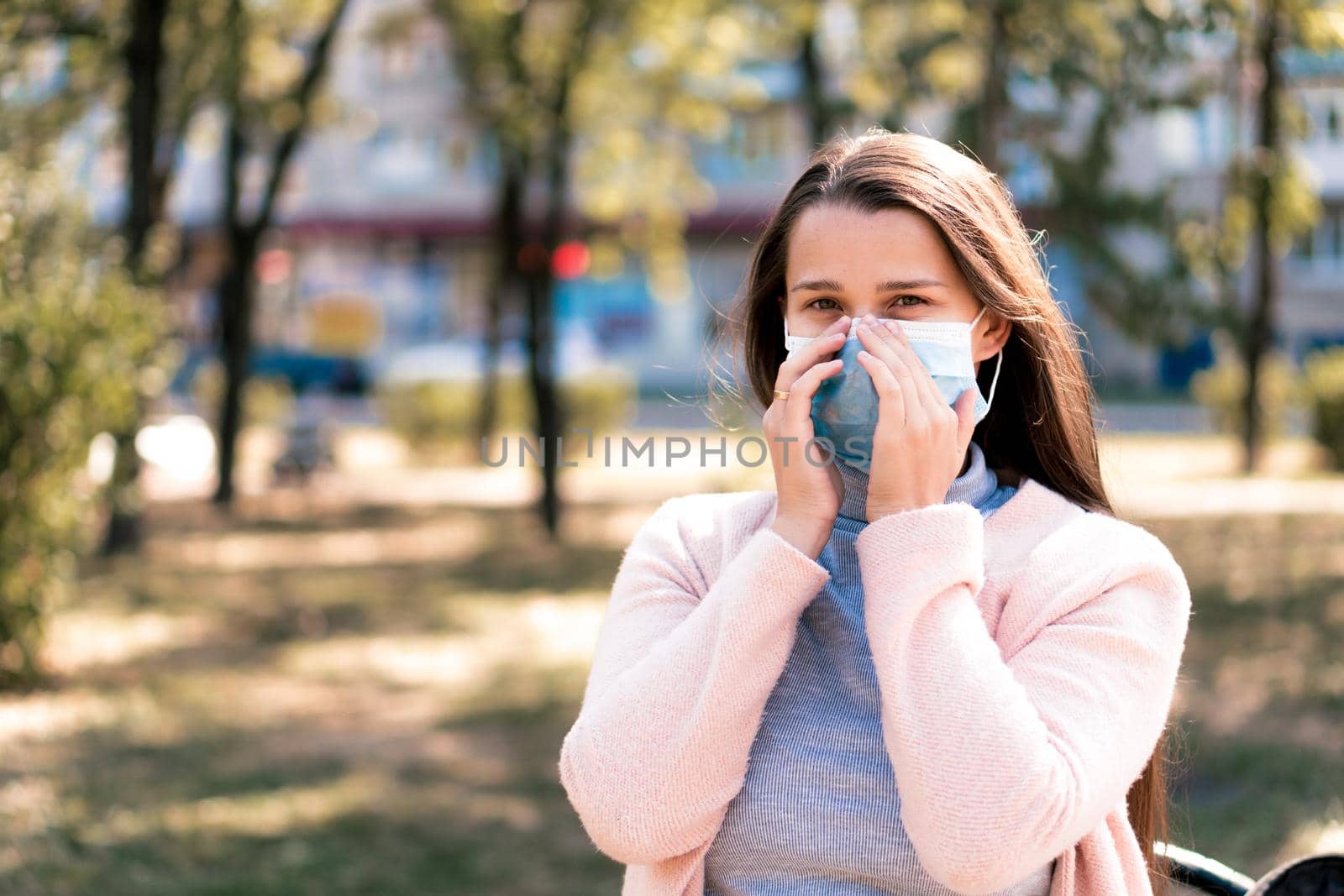 care, infants, spring, coronavirus and quarantine concept - Young cute long haired woman European Caucasian Slavic appearance put on blue medical protective mask in midday sunlight backlight in park. by mytrykau