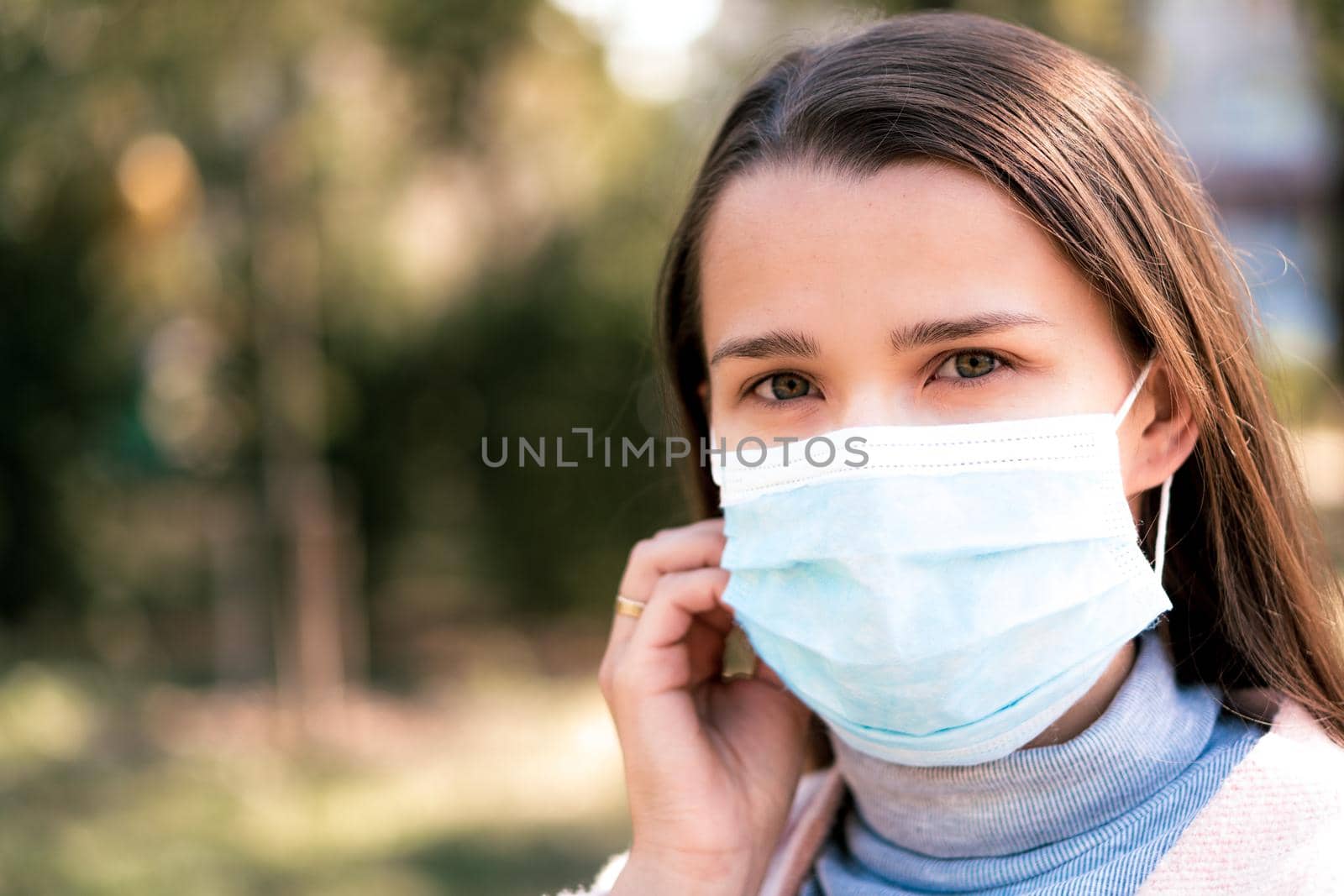 care, infants, spring, coronavirus and quarantine concept - Young cute long haired woman European Caucasian Slavic appearance put on blue medical protective mask in midday sunlight backlight in park. by mytrykau