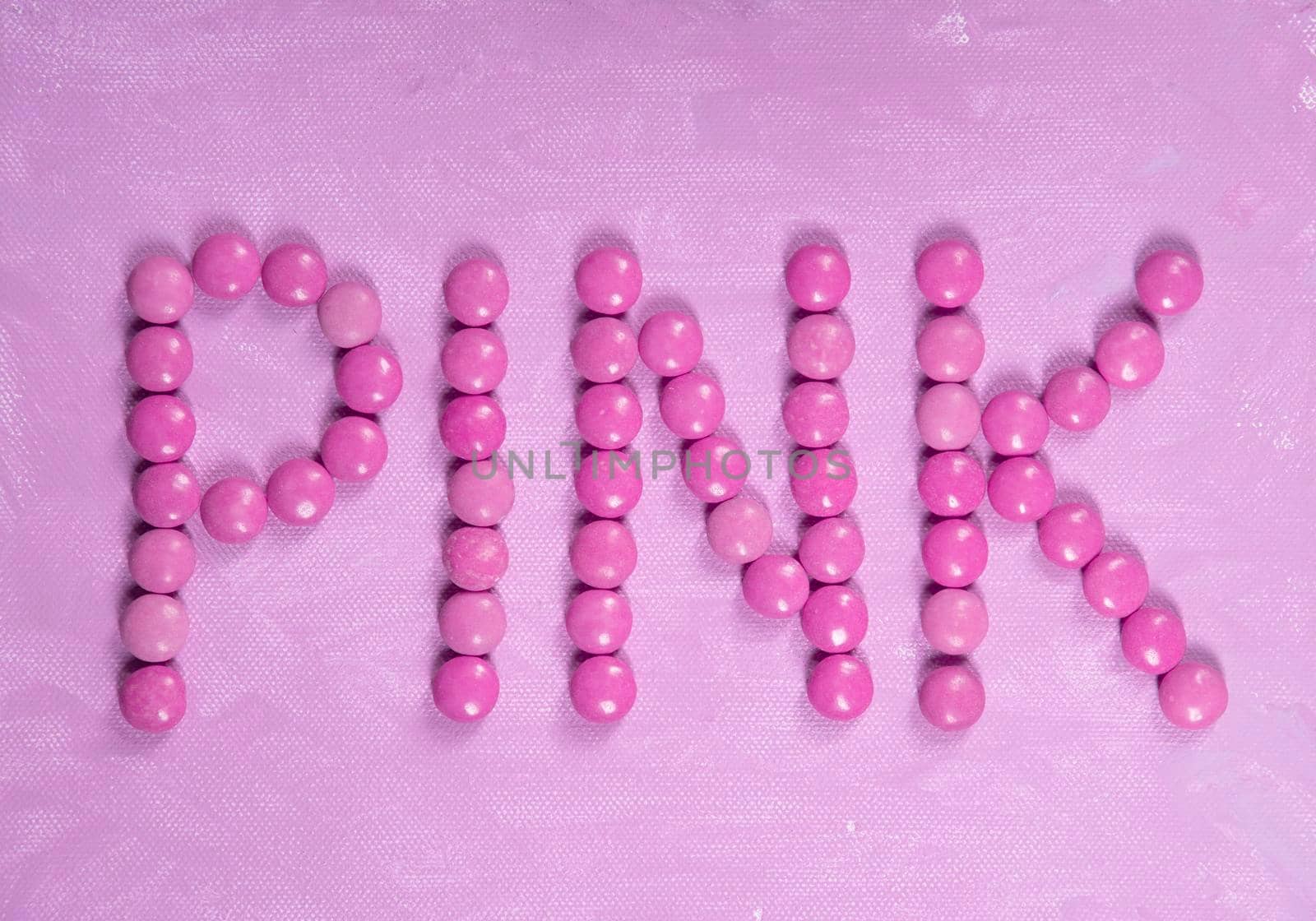 the word pink is written with pink sweets candies, on the pink background by KaterinaDalemans