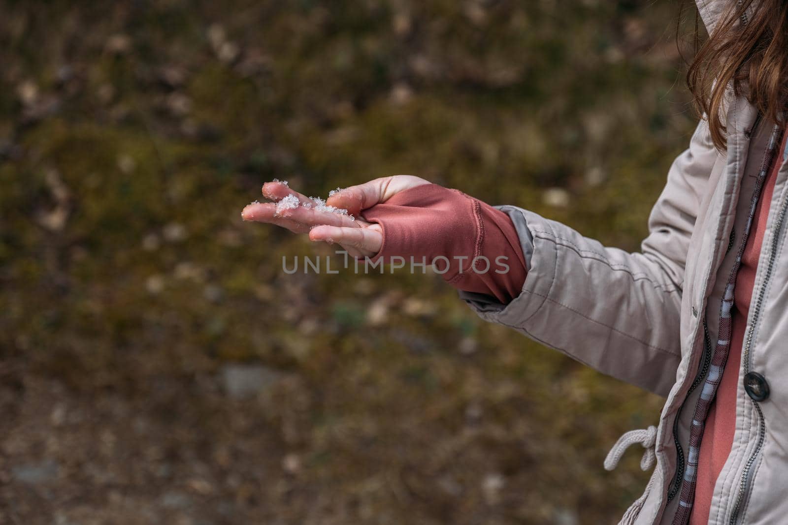 A woman wearing thumbhole jumper and holding melting snow in her hand during hiking in spring