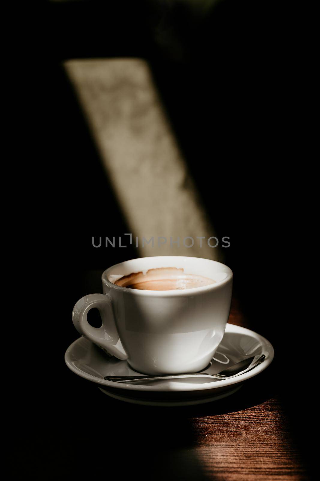 White cup of coffee on a wooden table in the sun a spoon for coffee foam in a cup