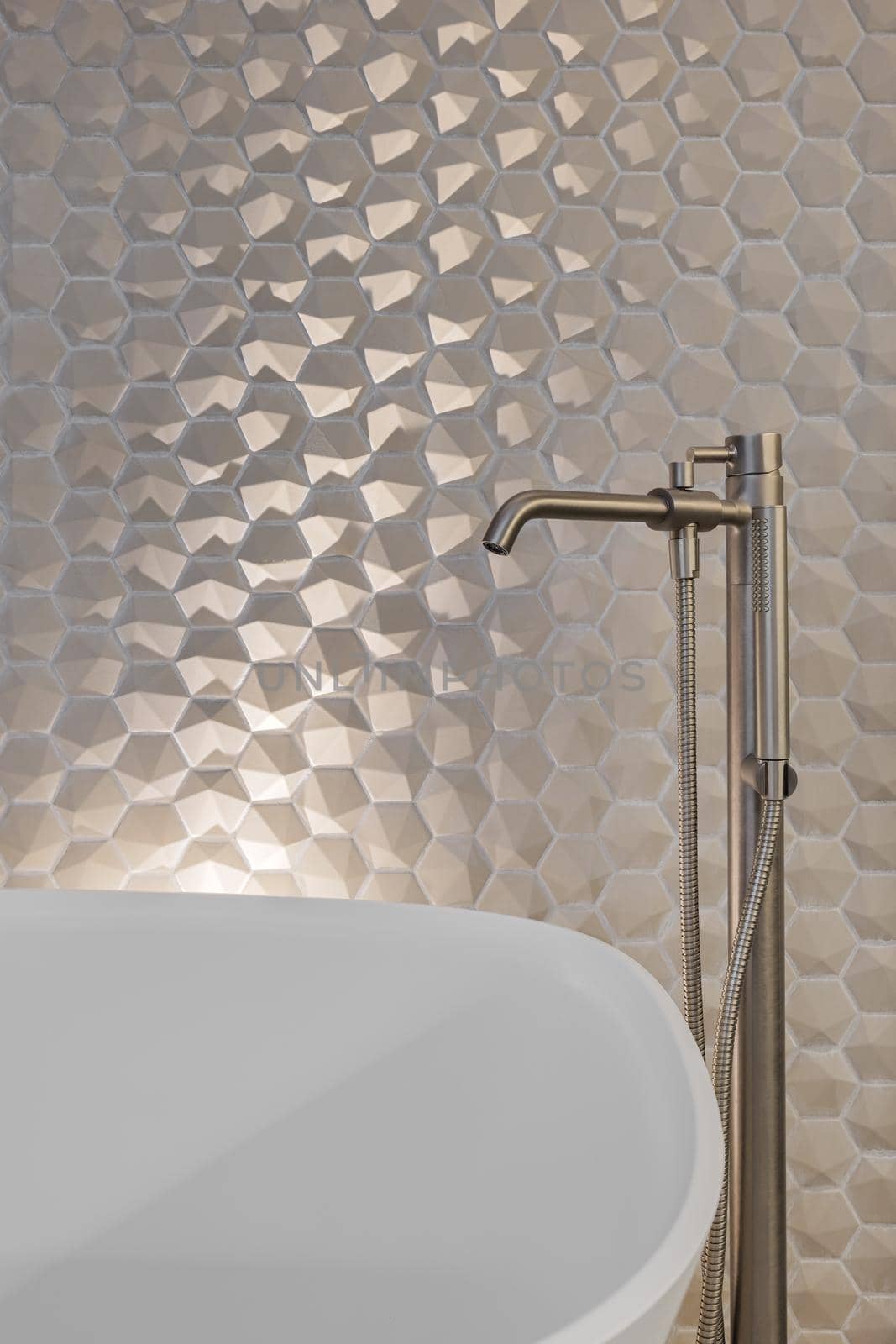 Metal faucet and shower in bathroom with hexagon tiles and white bath tub.