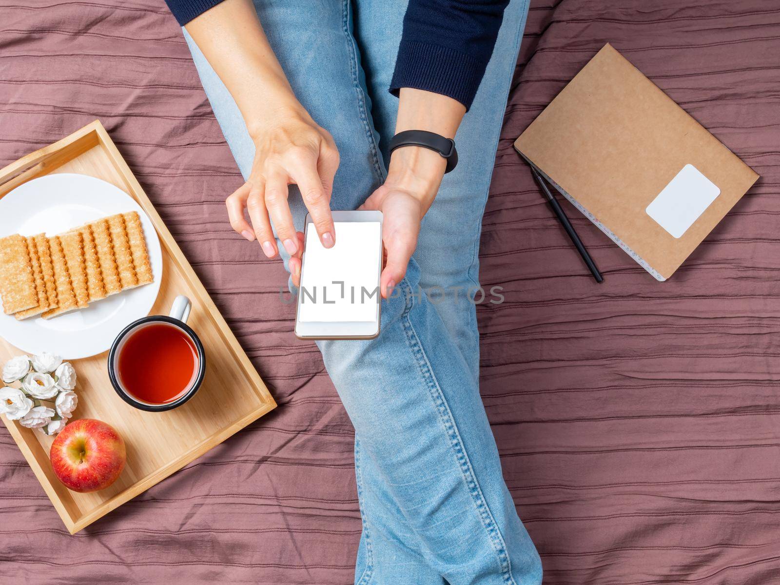 mockup with woman with smartphone, touching the screen, home furnishings, bed, flat lay.