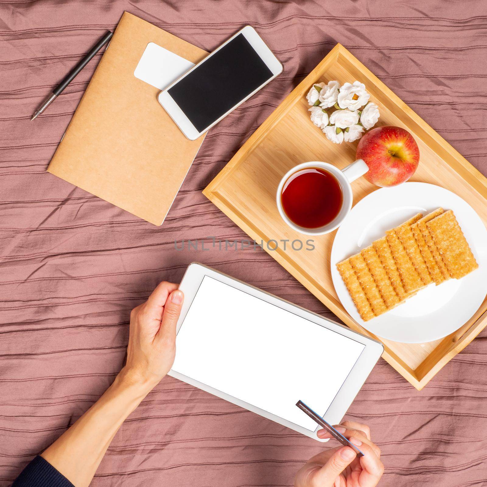 Woman lying on bed, drinking tea and looking at tablet, pay for purchases, online shopping by NataBene