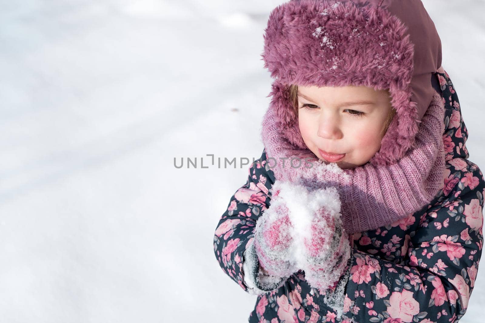 Winter, games, family, childhood concepts - close-up portrait authentic little preschool minor 3-4 years girl in pink hat warm clothes have fun smiles in snowy frosty weather. Funny kid eat taste snow by mytrykau