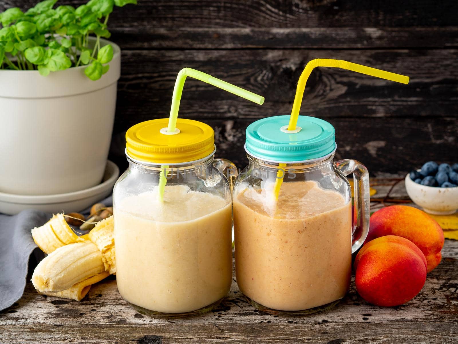 banana peach nectarine smoothie in two jars, fresh fruit milkshakes on the old dark rustic wooden table, side view