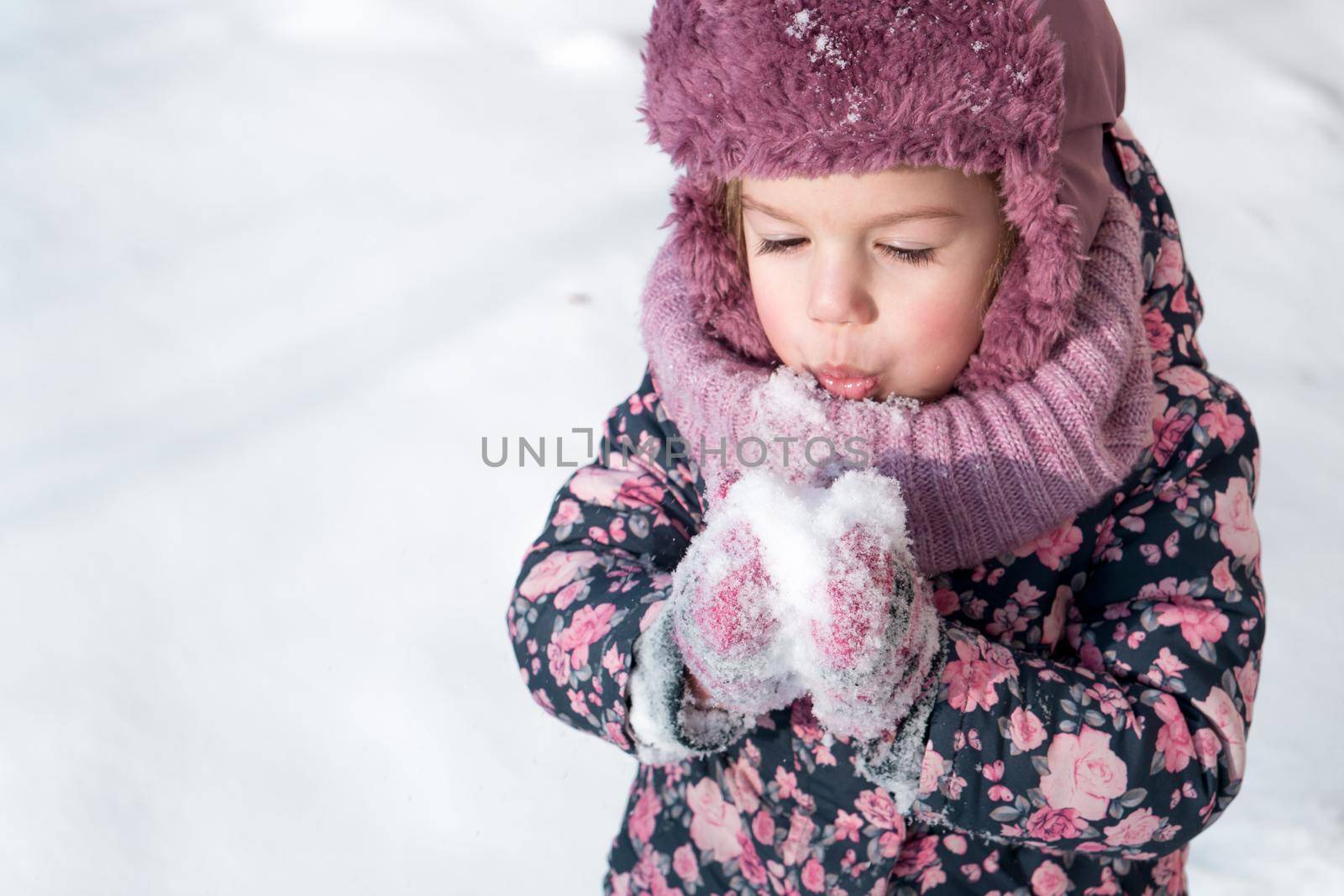 Winter, games, family, childhood concepts - close-up portrait authentic little preschool minor girl in pink hat warm clothes have fun smiles in cold frosty weather day. Funny kid blow on white snow by mytrykau