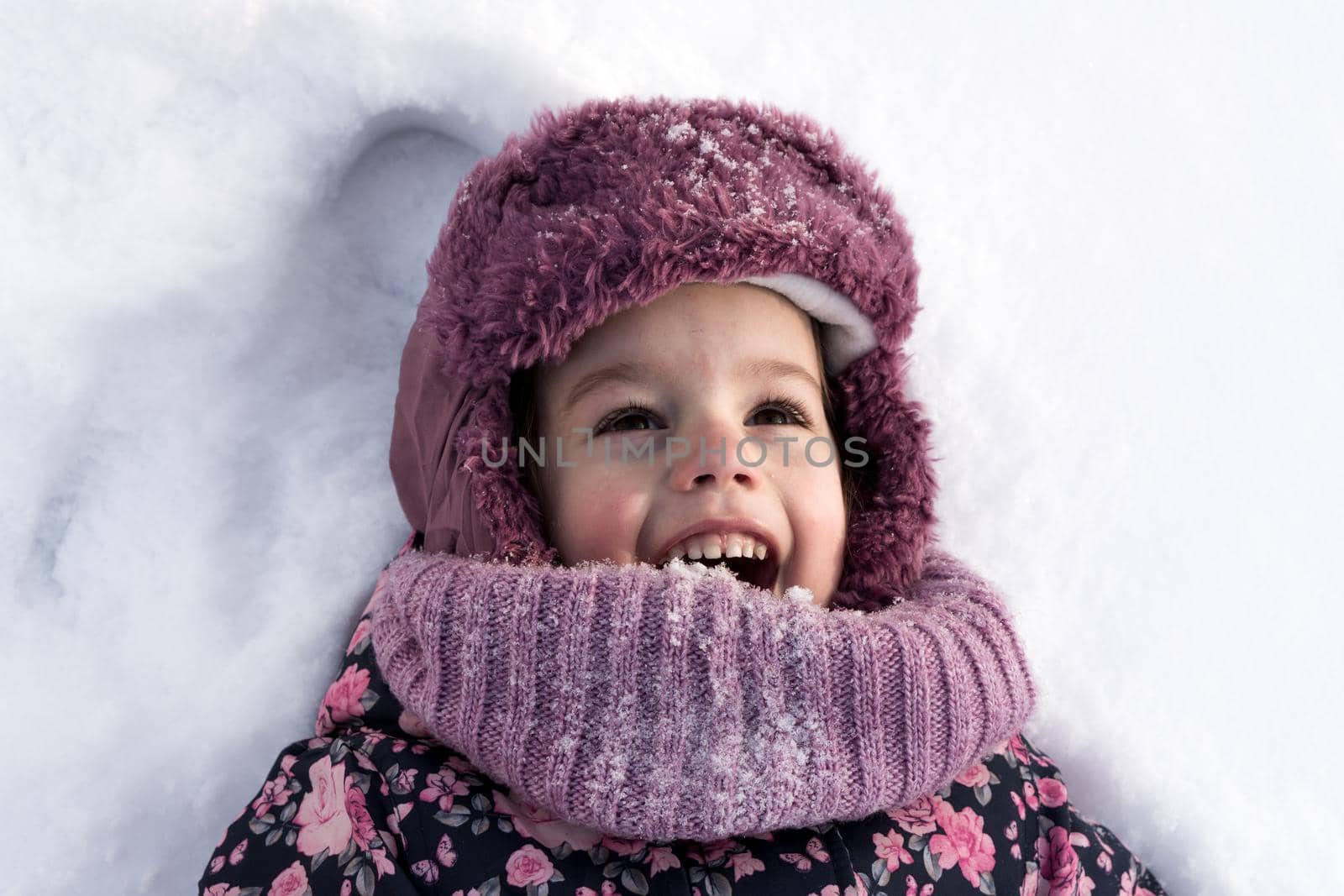 Winter, family, childhood concepts - close-up portrait authentic little preschool girl in pink clothes smile laugh shout with open mouth laying on snow in frosty weather day outdoors. Funny kid face by mytrykau