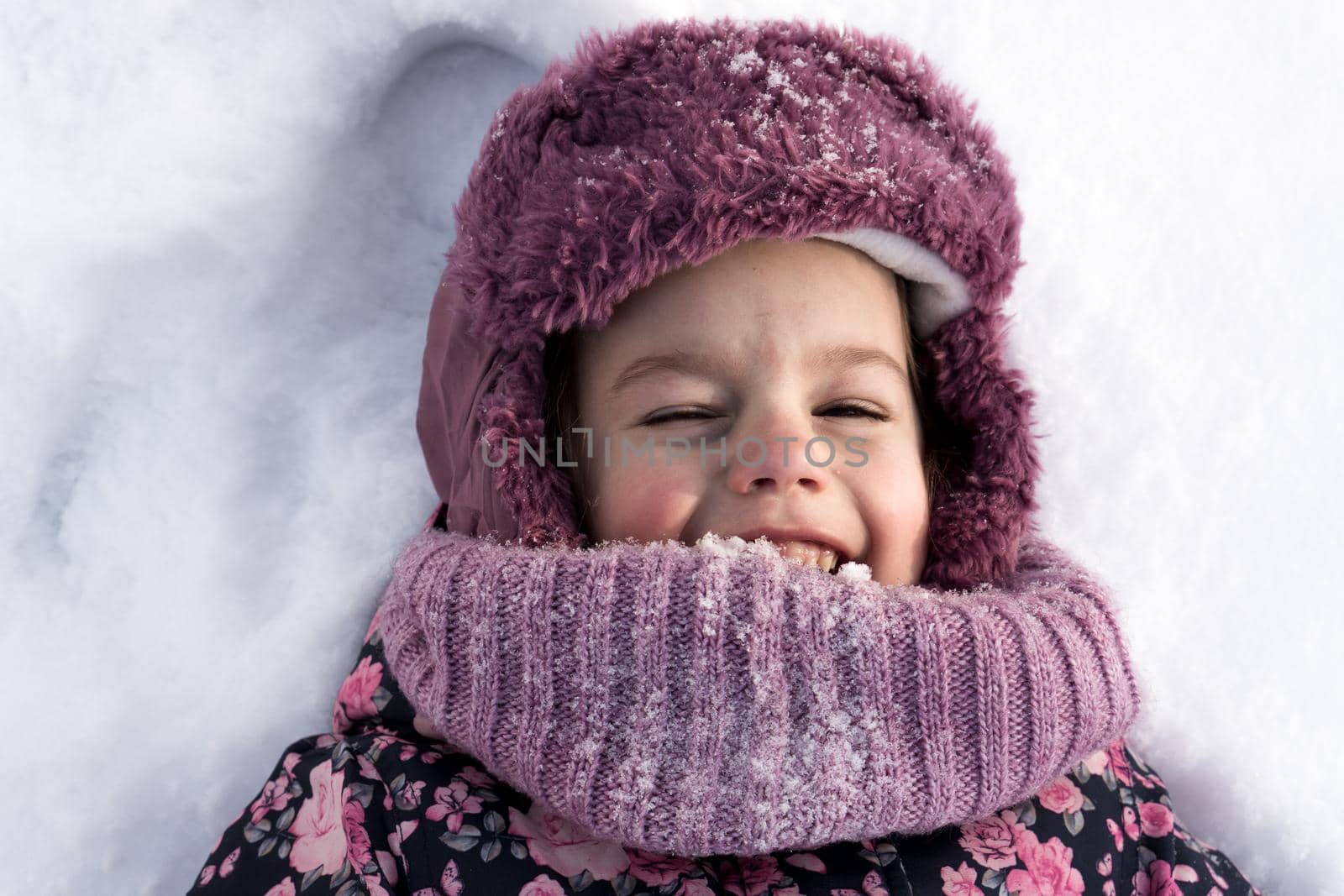 Winter, family, childhood concepts - close-up portrait authentic little preschool minor girl in pink clothes smile laugh closing eyes laying on snow in frosty weather day outdoors. Funny kid face by mytrykau