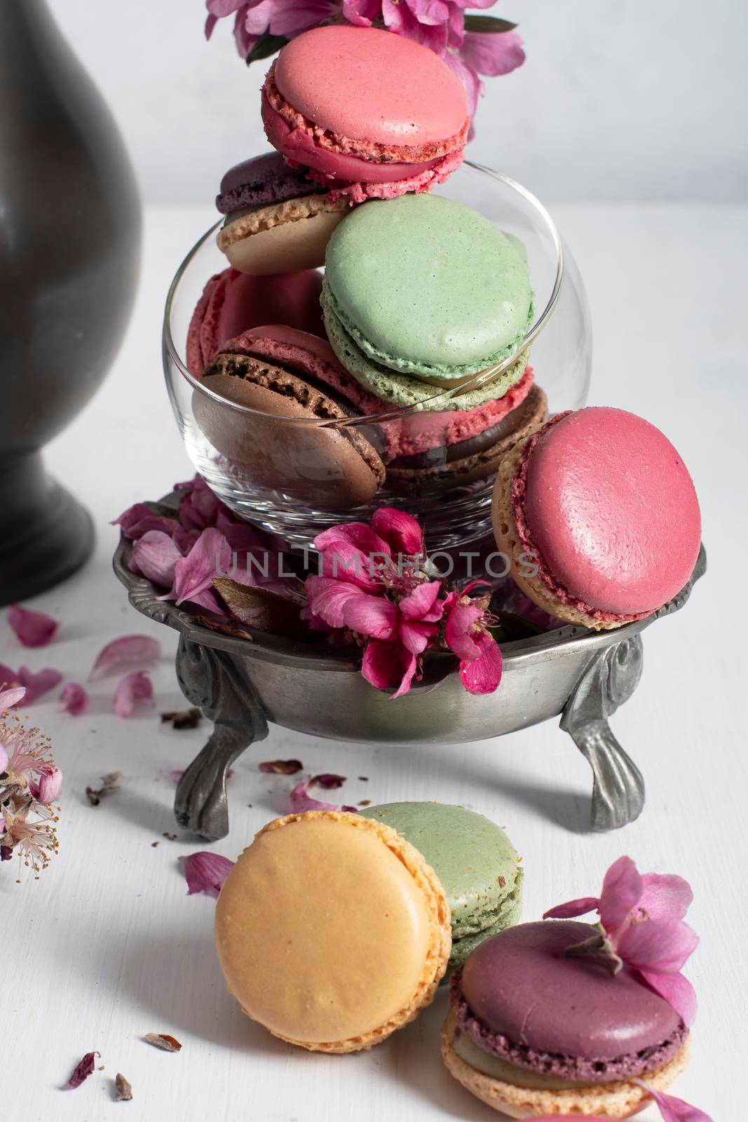 spring still life with colored macaroons and pink apple tree flowers in a pewter vase, colorful sweet food close up. High quality photo