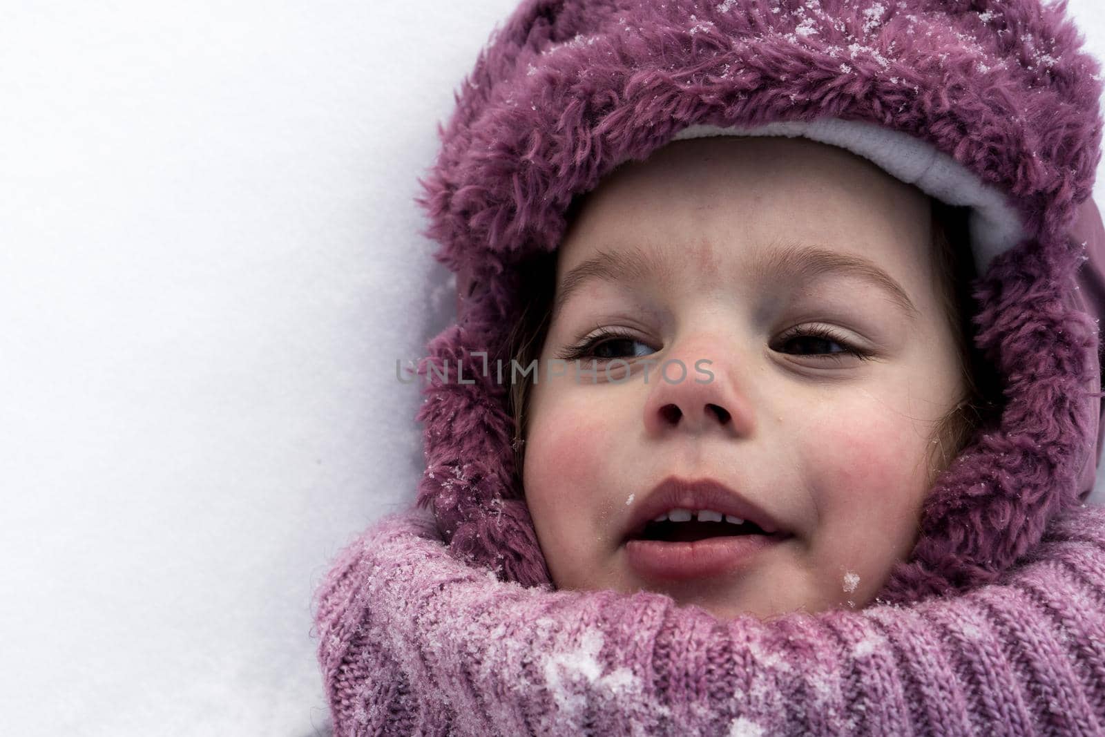 Winter, family, childhood concepts - close-up portrait authentic little preschool girl in pink clothes smile laugh shout with open mouth laying on snow in frosty weather day outdoors. Funny kid face.