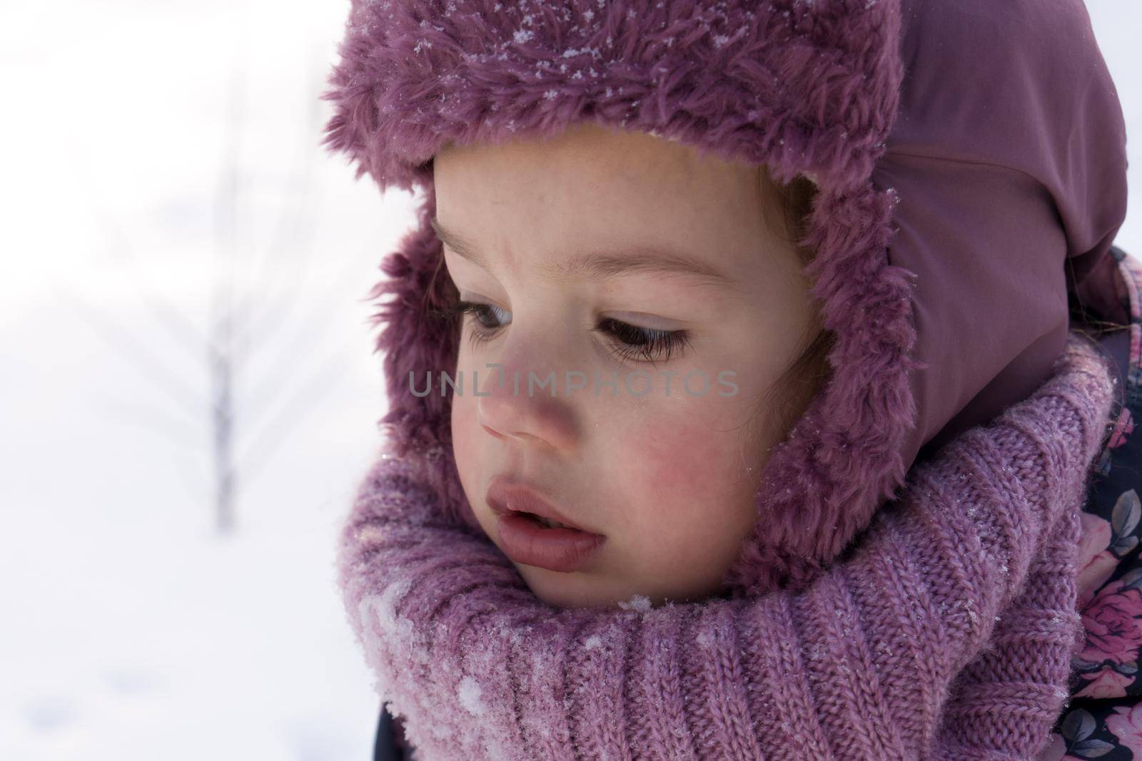 Winter, family, childhood concepts - close-up portrait authentic little preschool minor girl in pink look around in snowy frosty weather. surprised mysterious worried kid face outdoors. copy space by mytrykau