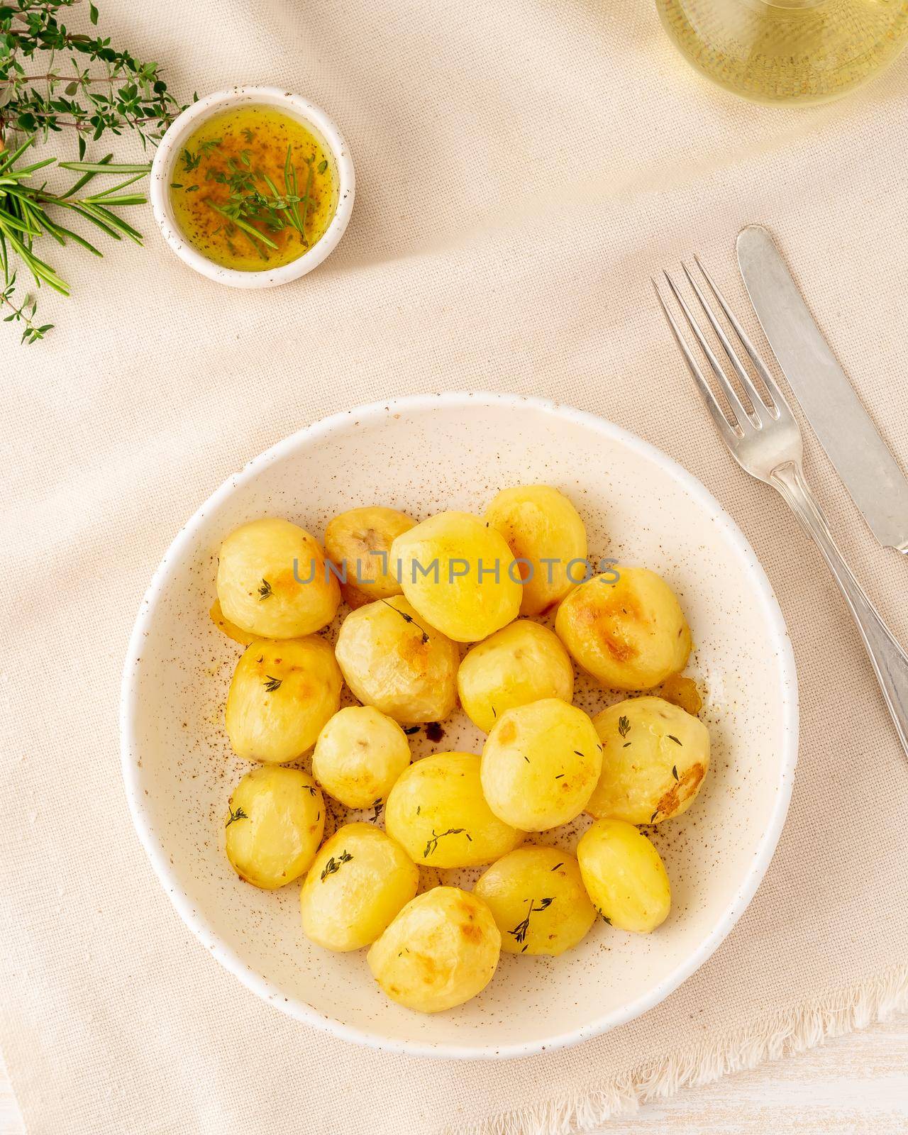 baked in oven with spices round whole potato tubers in plate on white textile background, vertical, top view by NataBene