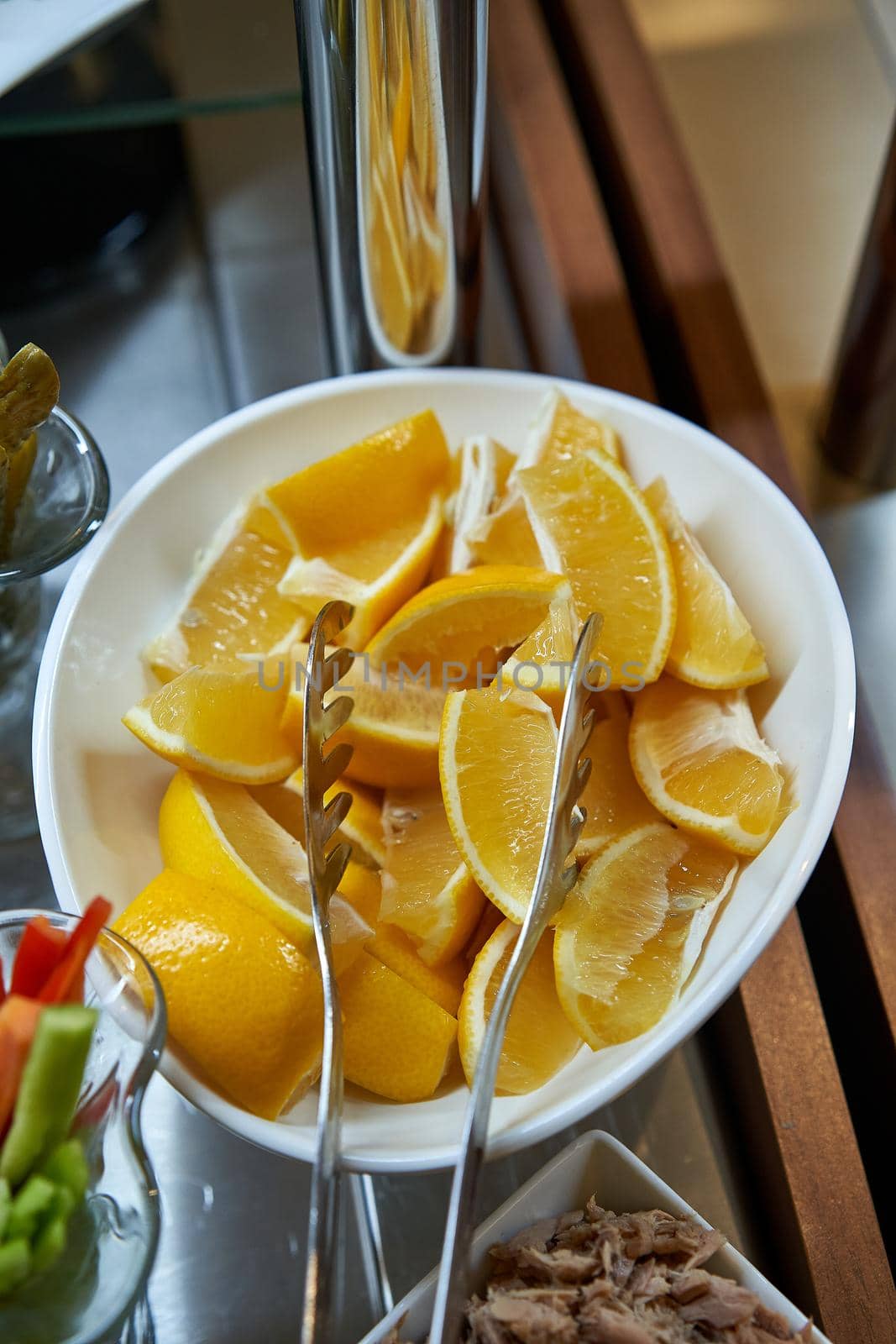 Lemon wedges in a white bowl with tongs for food close-up