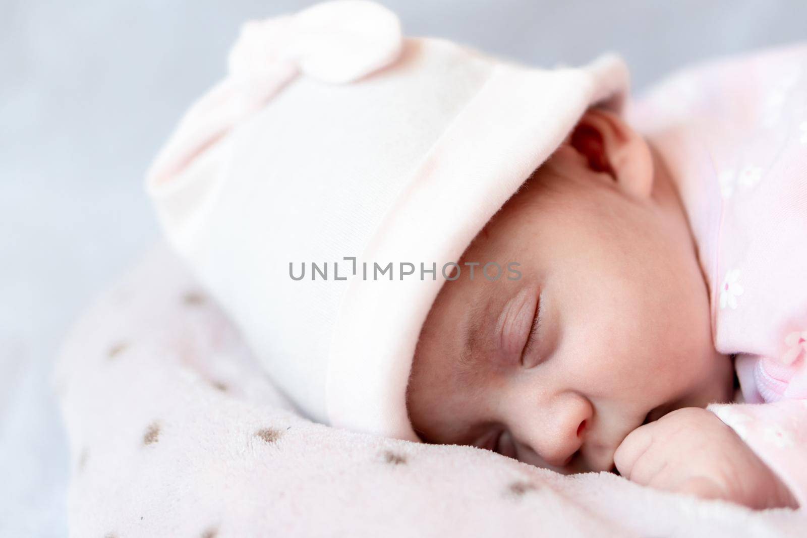 Childhood, care, motherhood, health concepts - Close up Little peace calm newborn baby girl in pink hat sleeps resting take deep nap laying on tummy on soft warm blanket pilow nest with close eyes.