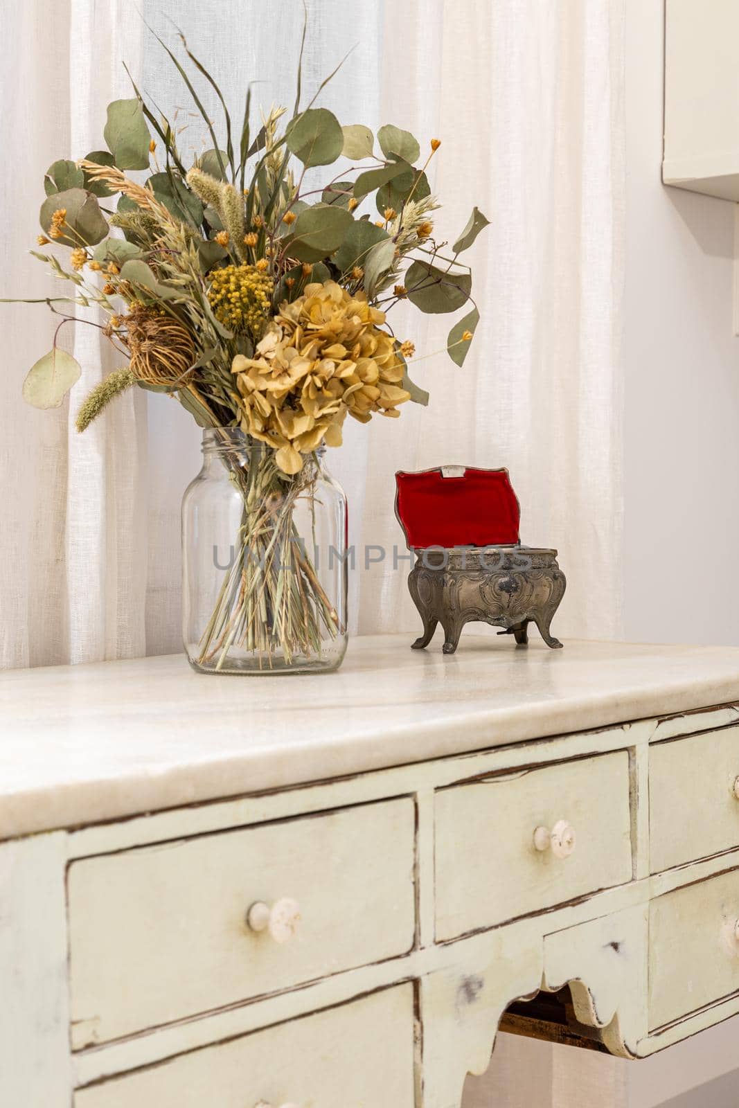 A bouquet of dried flowers and vintage jewelry box placed on retro style furniture