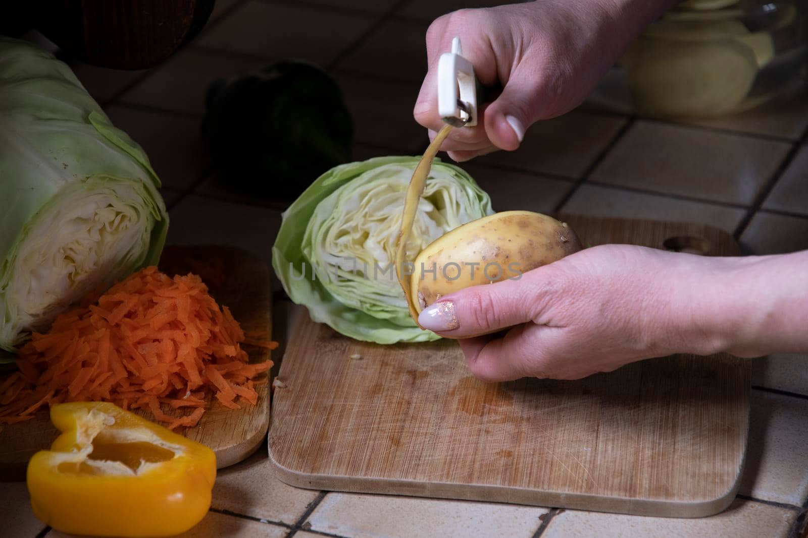 a woman peels potatoes in the kitchen against the background of fresh vegetables, ingredients for step by step cooking soup. High quality photo