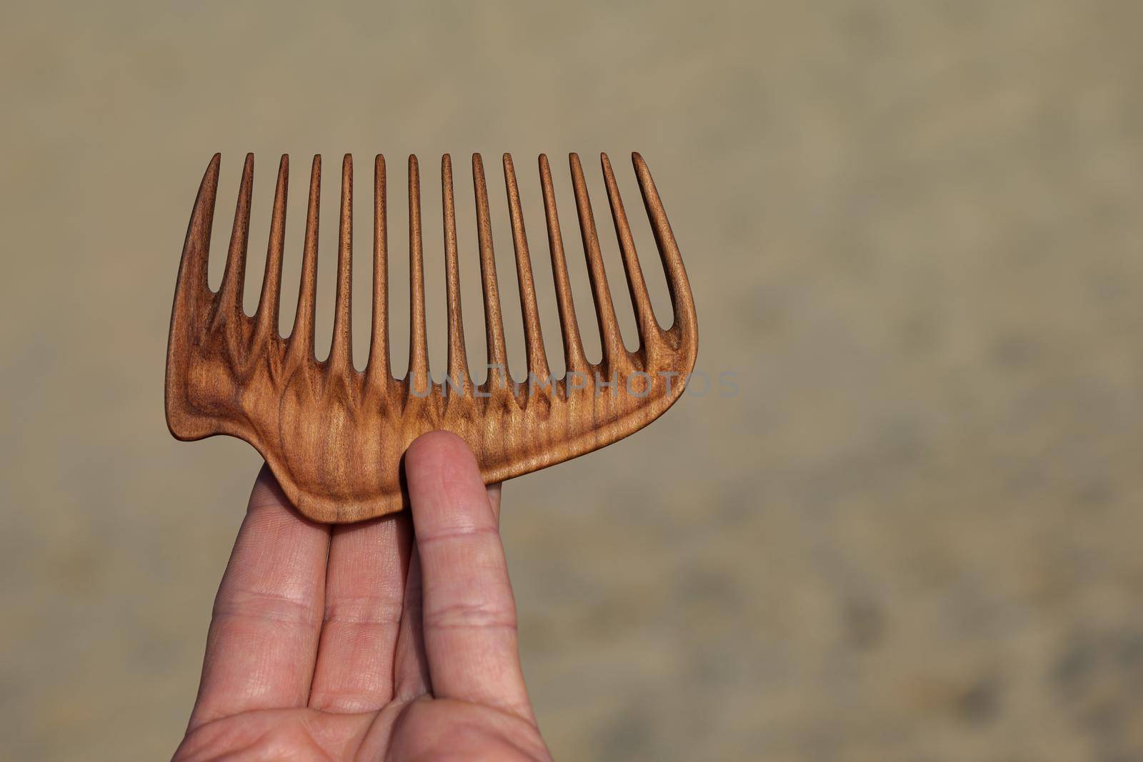 A hand holding natural wooden comb made of pear tree for scalp massage and aroma combing by apavlin