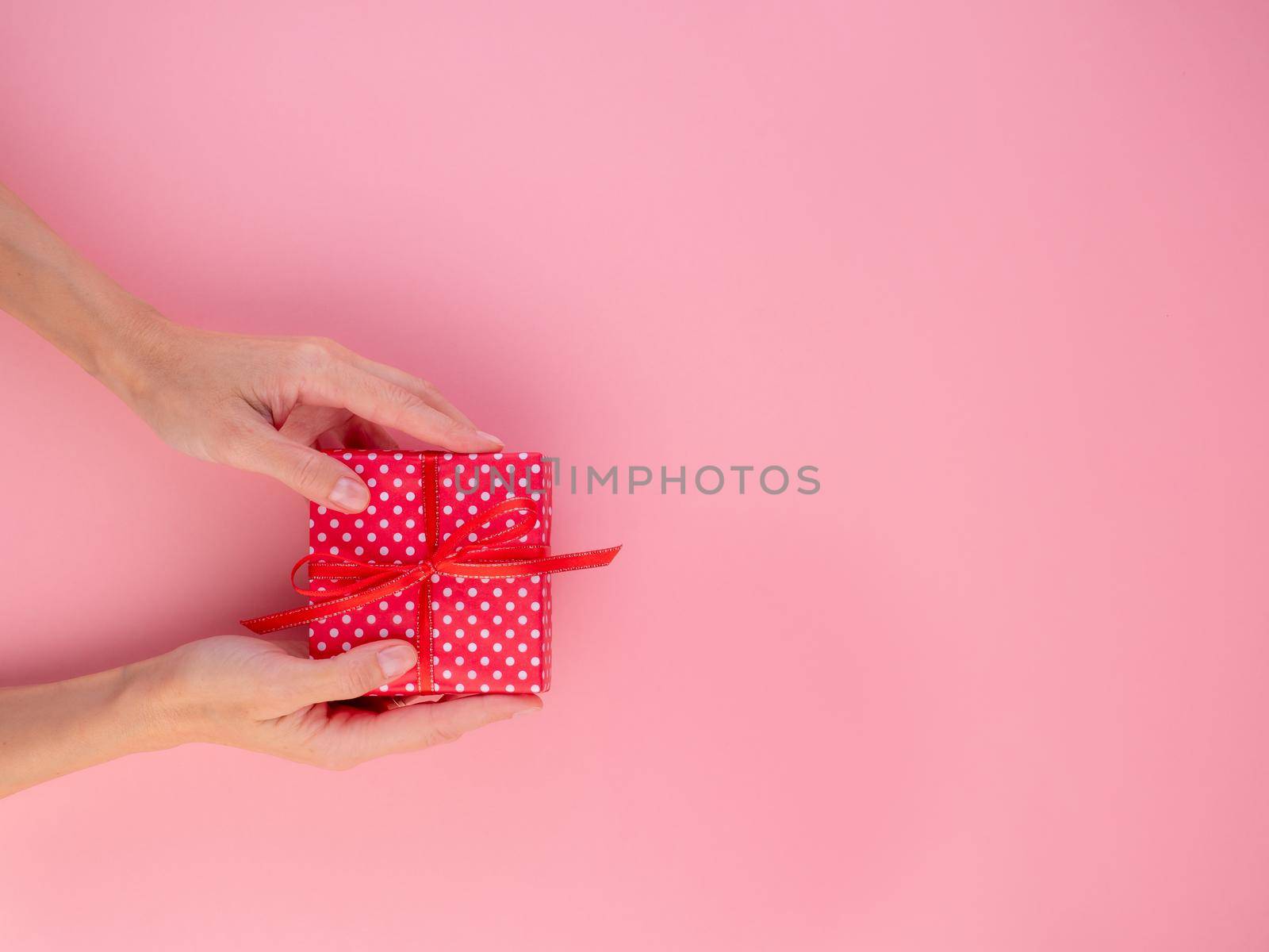 woman holding a gift in a red gift box with a bow, pink background, top view, empty space for text.