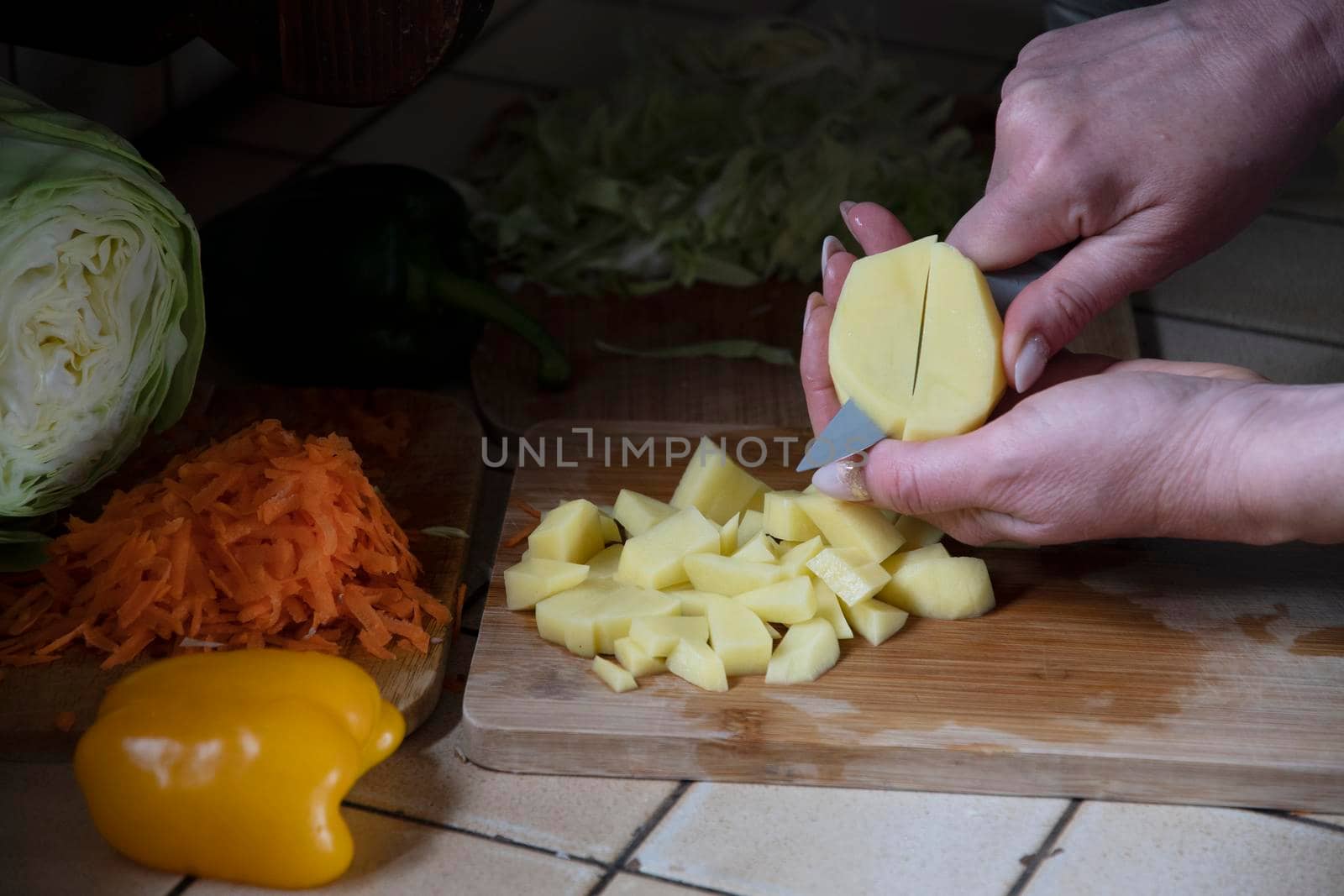 a woman cuts potatoes in the kitchen against the background of fresh vegetables, ingredients for step by step cooking soup. High quality photo