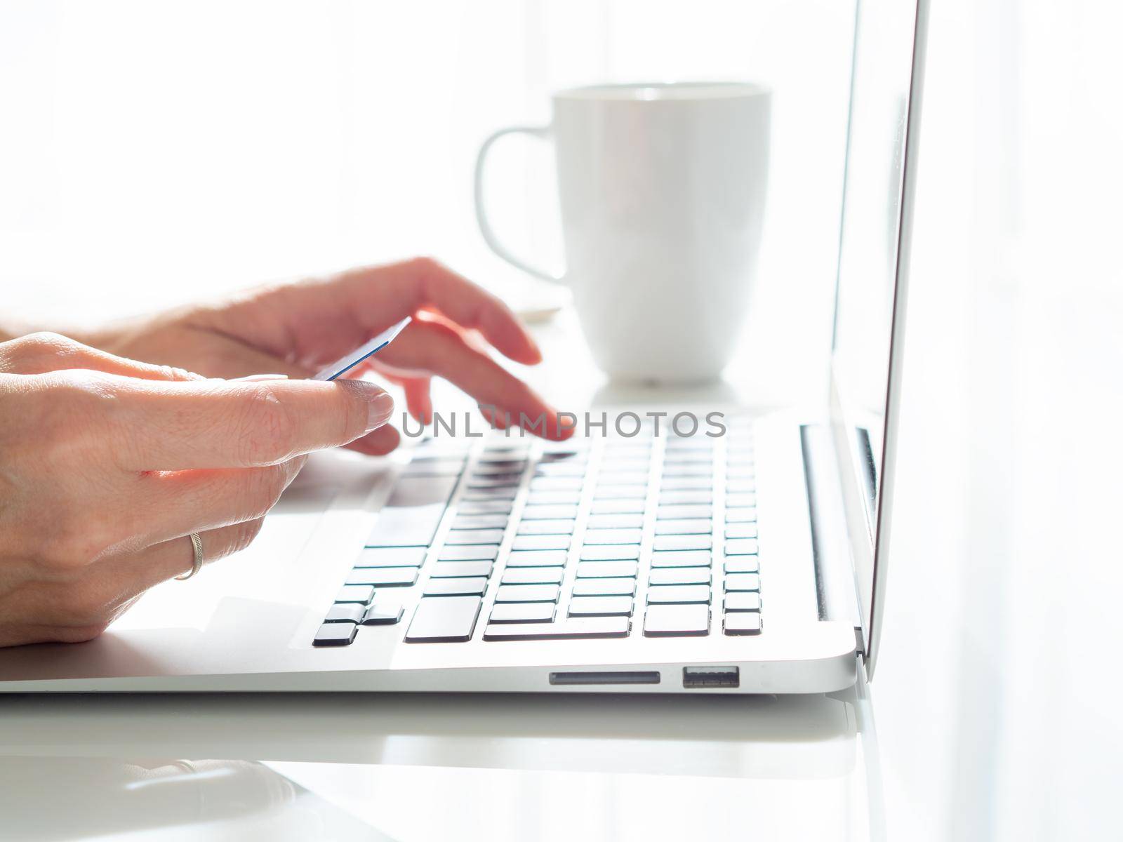 woman sitting at a table, drinking tea and looking at a laptop, pay for purchases by credit card, online shopping