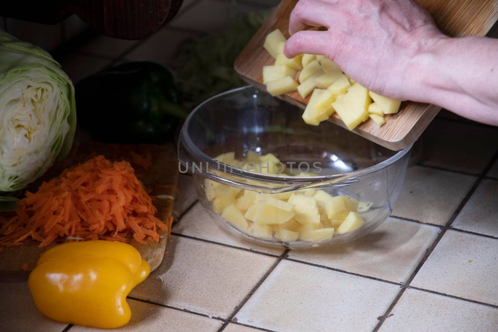 a woman cuts potatoes in the kitchen against the background of fresh vegetables, ingredients for step by step cooking soup. High quality photo