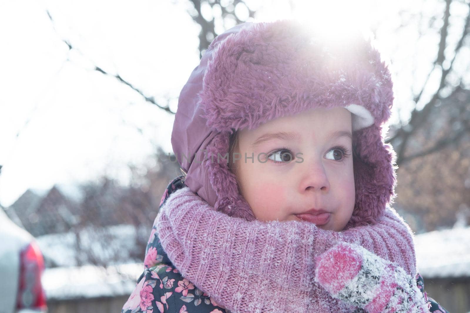 Winter, games, family, childhood concepts - close-up portrait authentic little preschool minor 3-4 years girl in pink hat look at camera posing smiles in snowy frosty weather. Funny kid eat taste snow by mytrykau