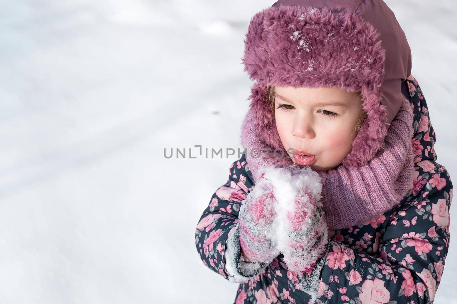 Winter, games, family, childhood concepts - close-up portrait authentic little preschool minor 3-4 years girl in pink hat warm clothes have fun smiles in snowy frosty weather. Funny kid eat taste snow by mytrykau