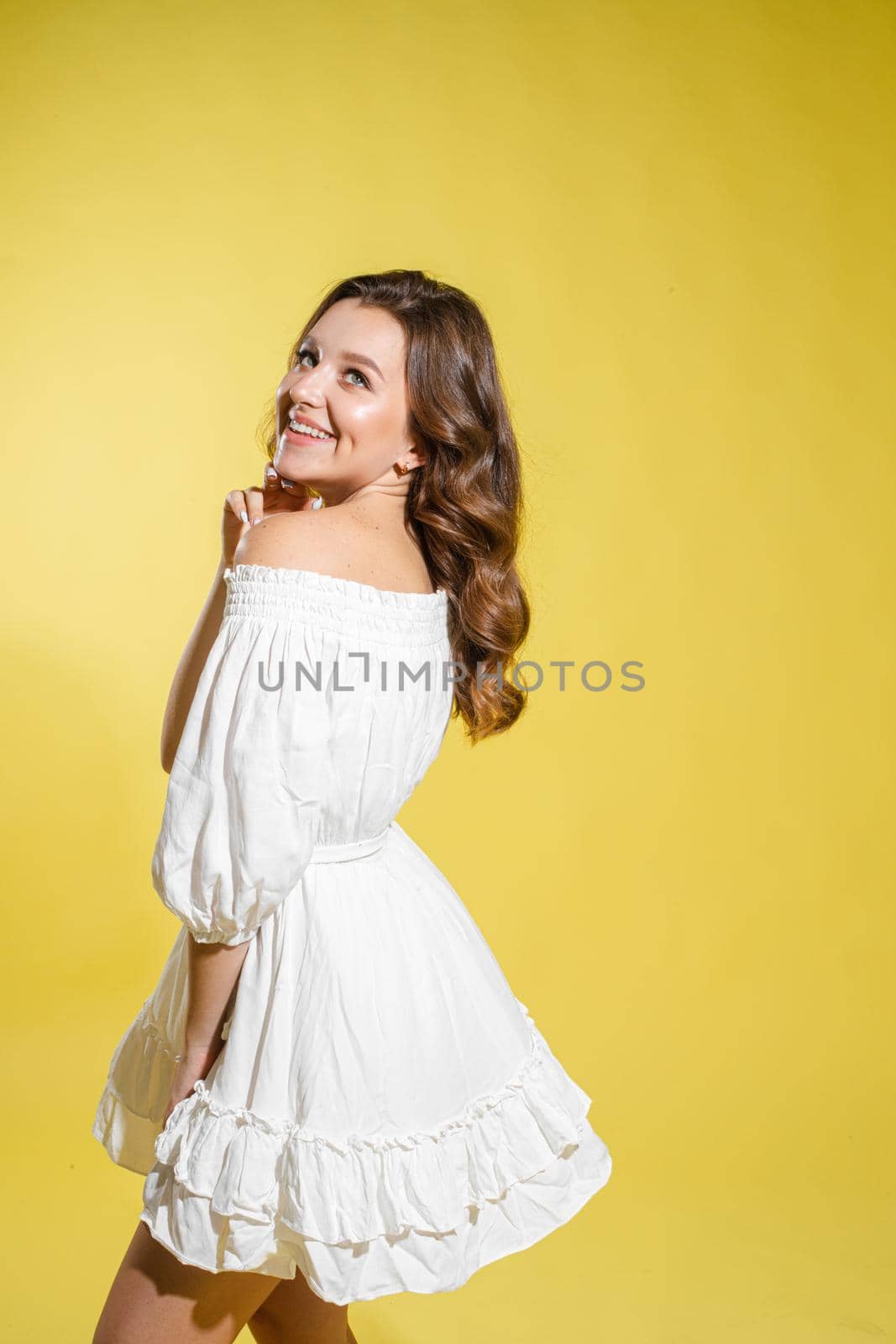 Beautiful bright woman in the studio on a yellow background in a white light dress smiling happy,