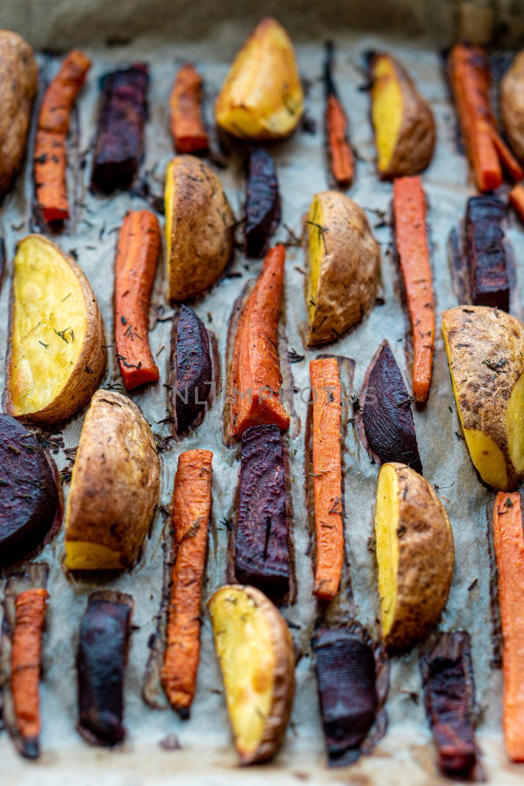 restaurant, vegetarianism, fast, healthy food, recipes concepts - Oven baked cut vegetables potatoes carrots, beets with seasoning dill. Roasted potatoes in jackets. Top view. Close up after cooking.